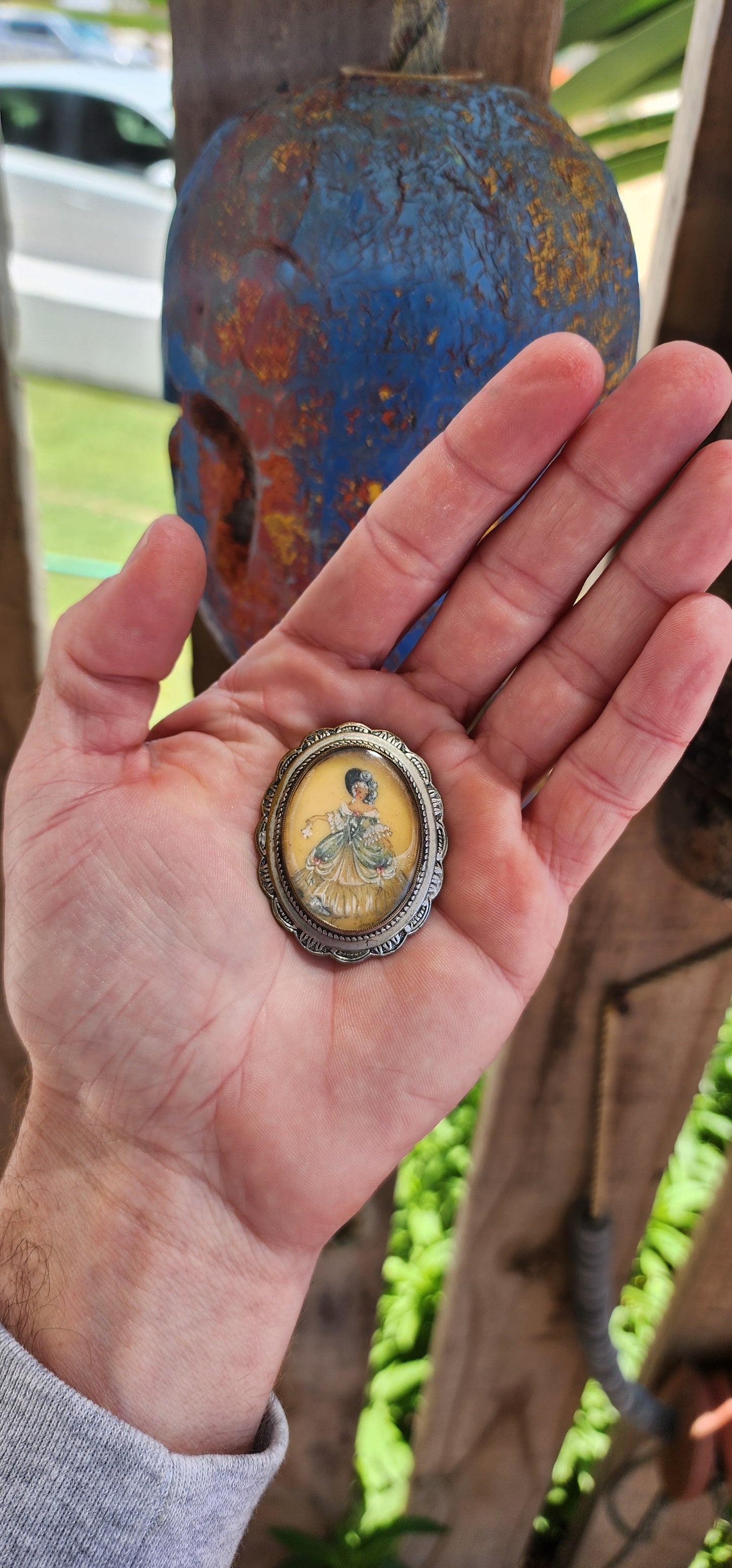 This brooch is an exquisite example of vintage craftsmanship, featuring a signed hand-painted miniature portrait encased in a silver-plated frame with a domed, convex glass cover.