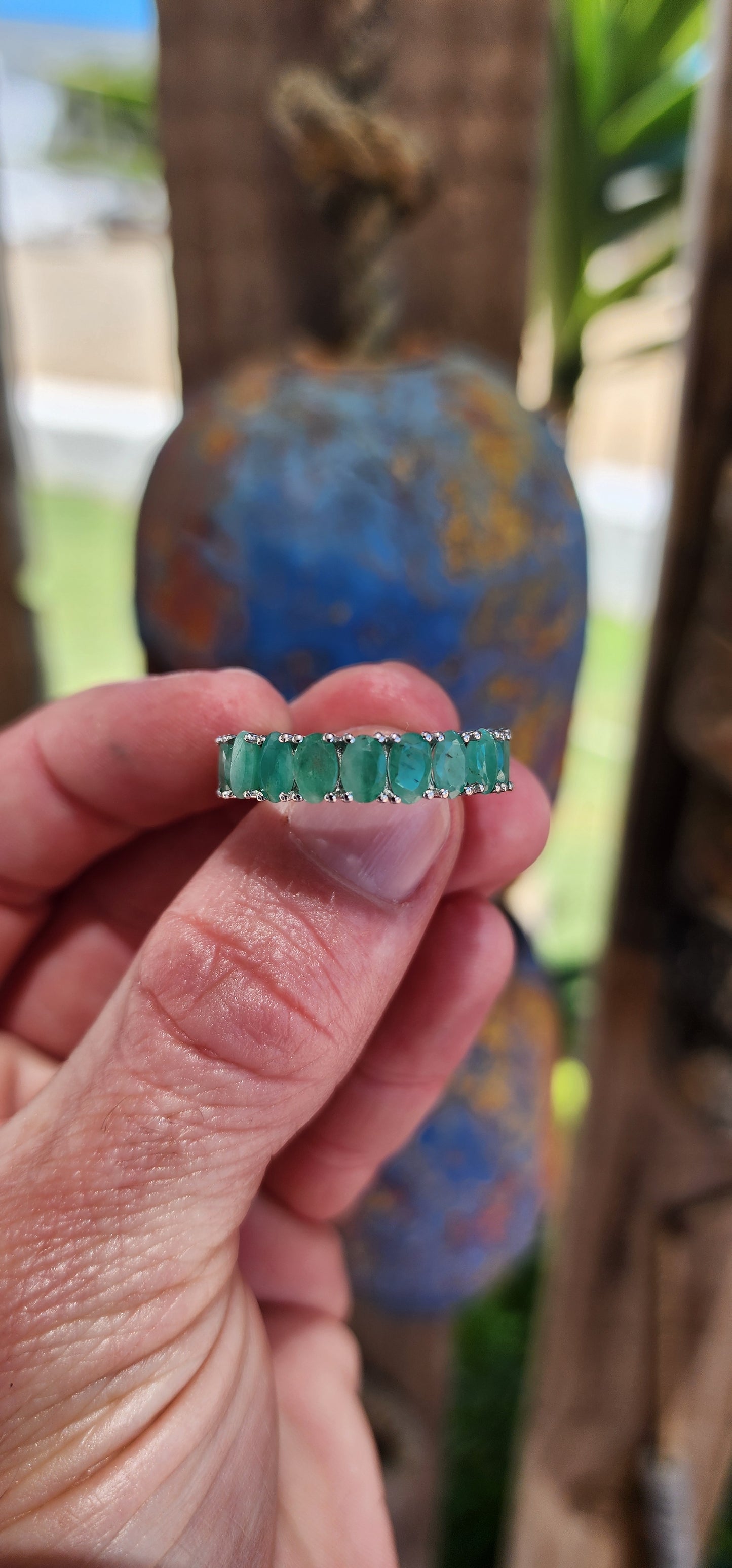 This stunning sterling silver full eternity ring is a true showstopper, set with 20 vibrant oval-cut emerald gemstones, each securely held in prong settings.