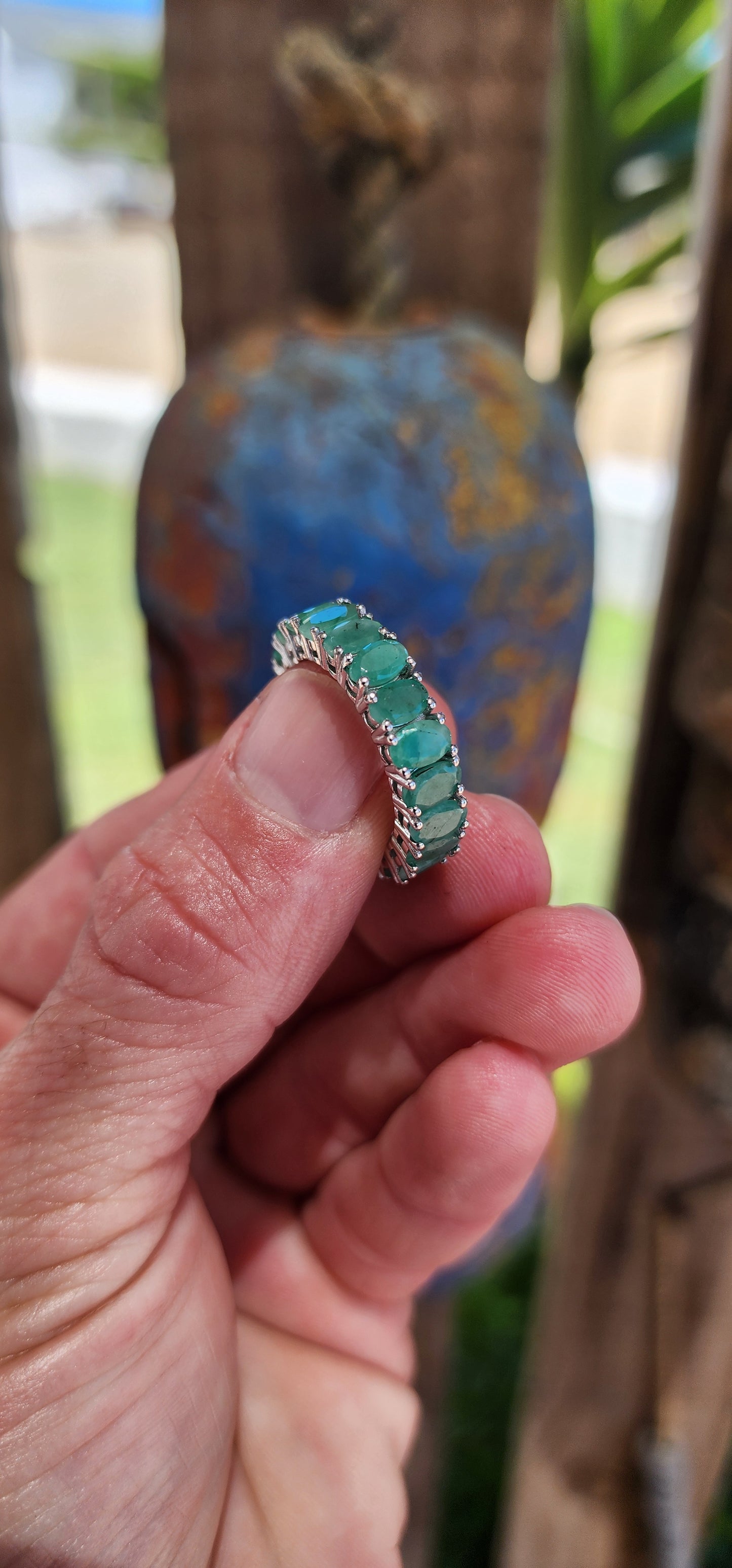 This stunning sterling silver full eternity ring is a true showstopper, set with 20 vibrant oval-cut emerald gemstones, each securely held in prong settings.