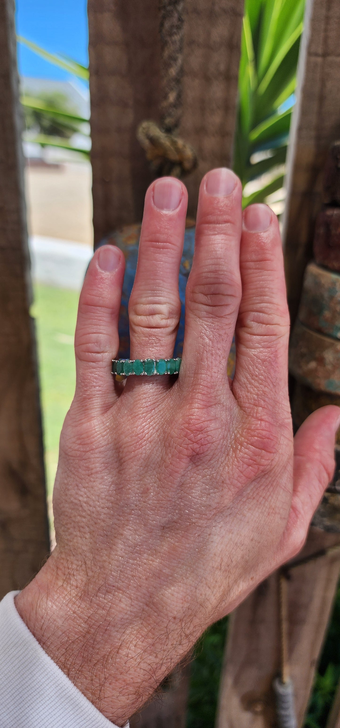 This stunning sterling silver full eternity ring is a true showstopper, set with 20 vibrant oval-cut emerald gemstones, each securely held in prong settings.