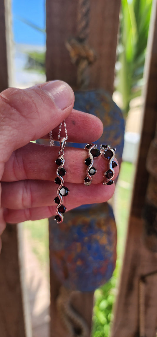 This sterling silver and garnet matching jewelry set is a testament to timeless craftsmanship and elegant design, composed of a pair of half-round push-in earrings with safety leverbacks and a gracefully matching pendant on an adjustable-length chain.