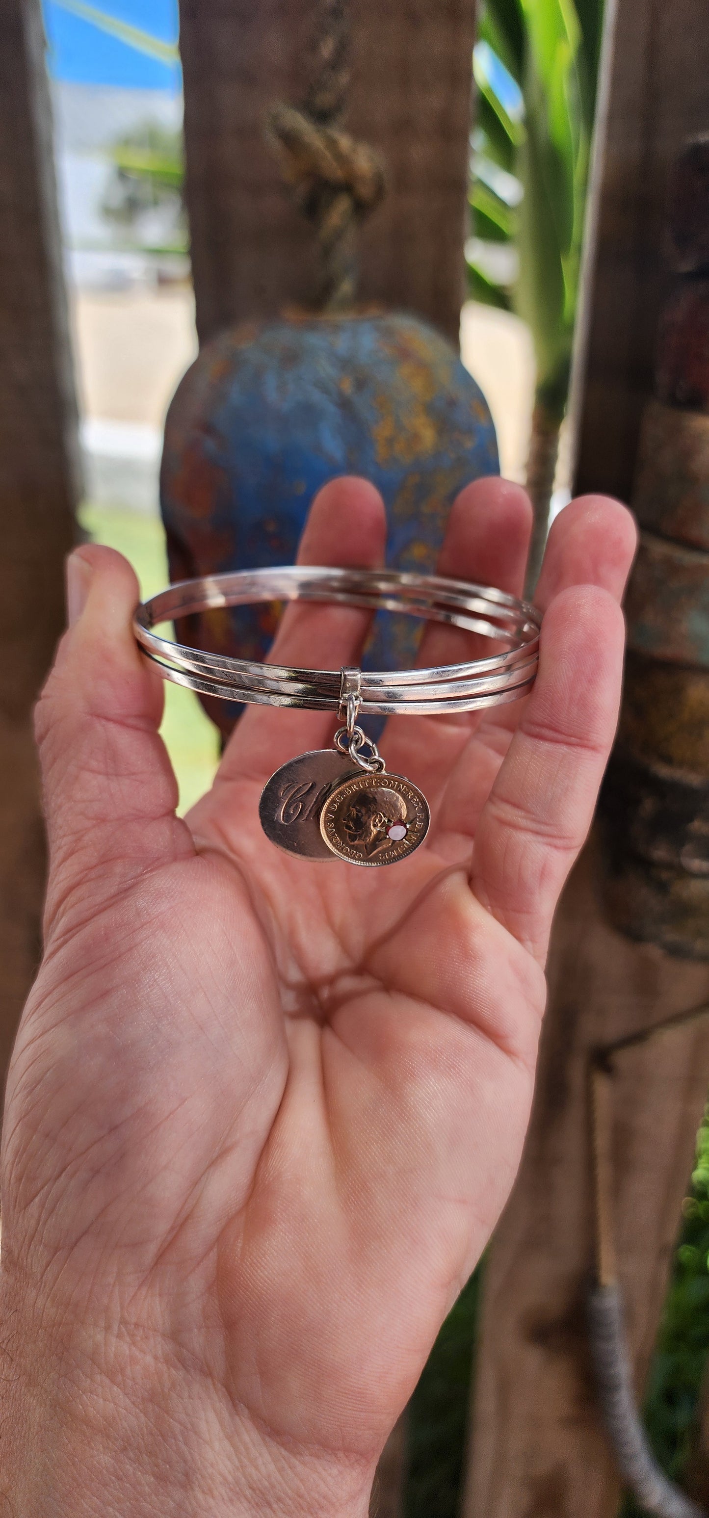 This antique sterling silver bangle, comprising a set of three hinged bangles joined together, beautifully incorporates two historically significant "love token" coin pendants, showcasing a rich blend of craftsmanship and sentimentality.