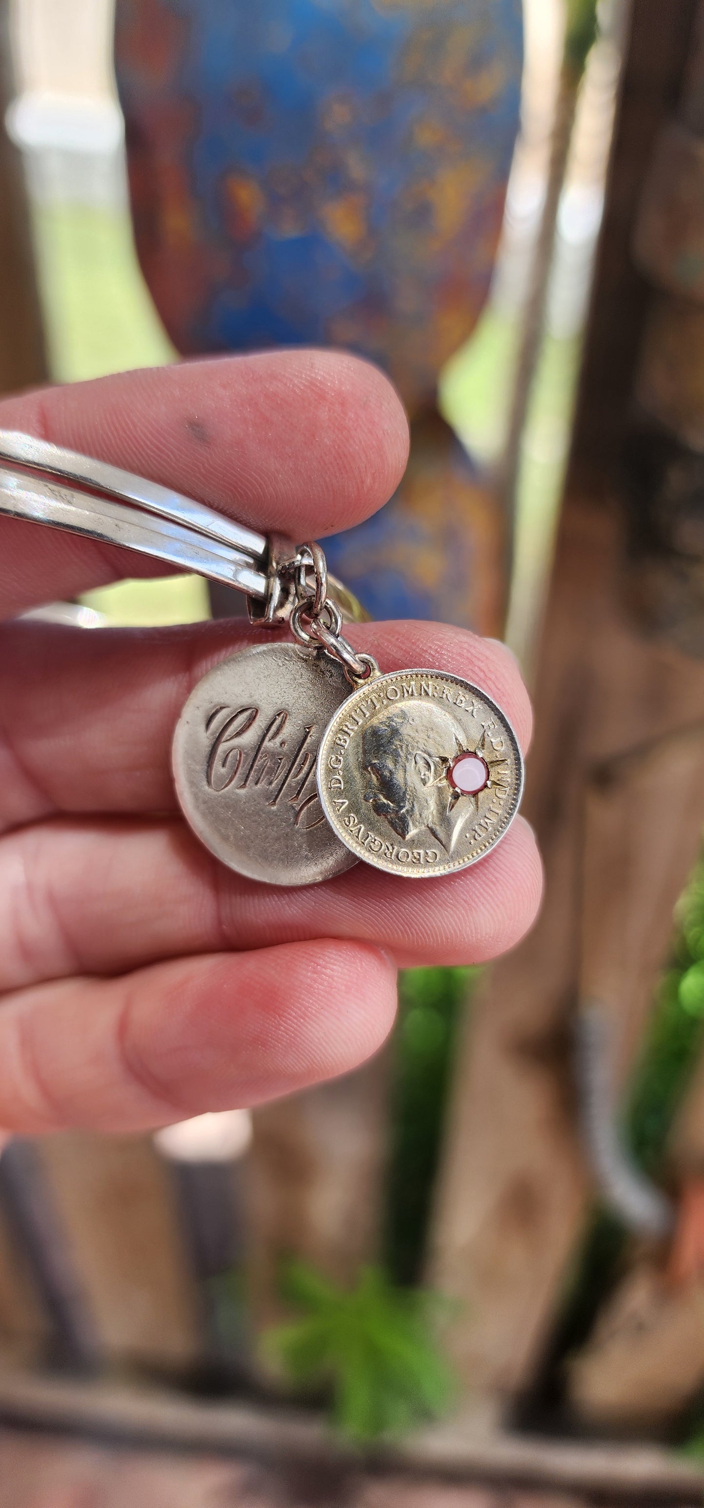 This antique sterling silver bangle, comprising a set of three hinged bangles joined together, beautifully incorporates two historically significant "love token" coin pendants, showcasing a rich blend of craftsmanship and sentimentality.