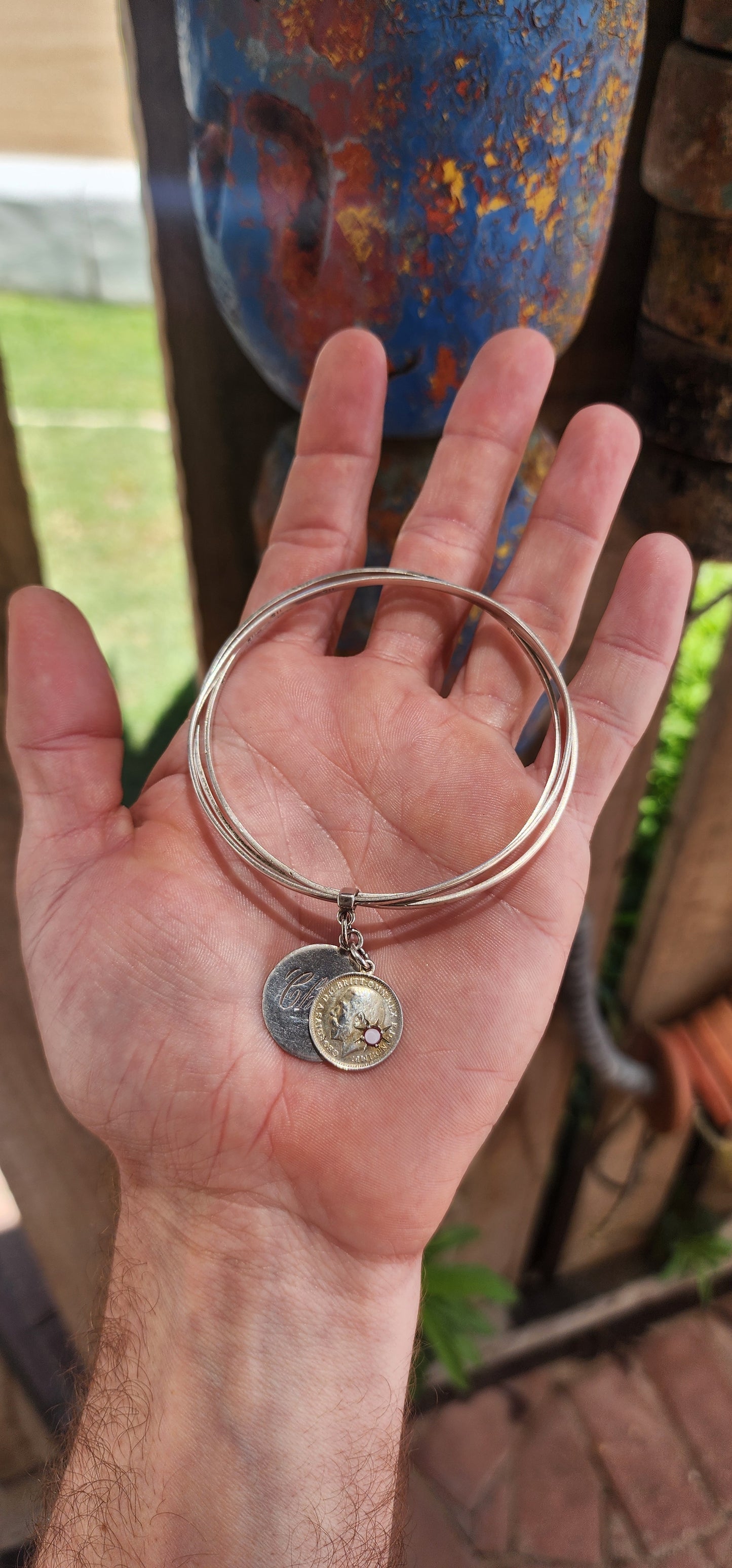 This antique sterling silver bangle, comprising a set of three hinged bangles joined together, beautifully incorporates two historically significant "love token" coin pendants, showcasing a rich blend of craftsmanship and sentimentality.