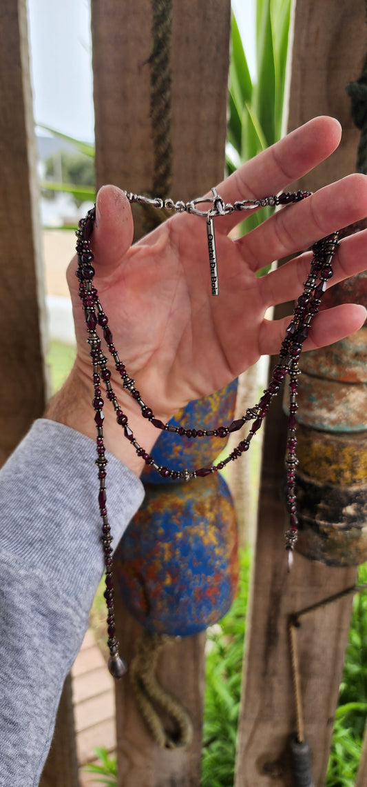 This exquisite artisan-crafted necklace is a stunning three-strand choker that seamlessly blends elegance with versatility. Its intricate design features genuine almandine garnet gemstone beads and sterling silver accents.