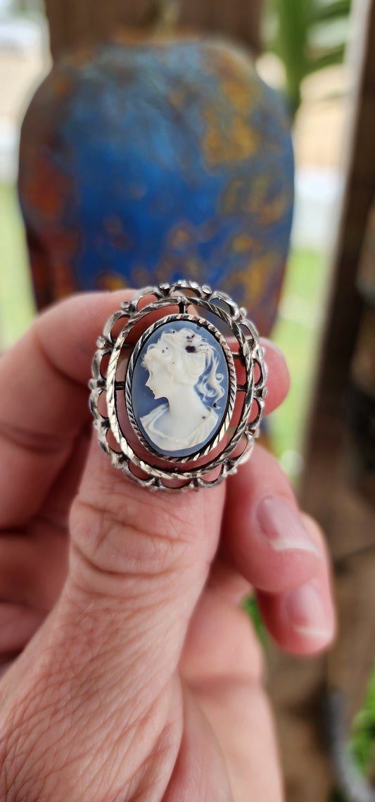 This is a lovely vintage sterling silver brooch featuring a delicate blue cameo crafted from resin.
The centerpiece is an oval blue cameo depicting a classic profile of a lady, likely inspired by Victorian-era motifs.