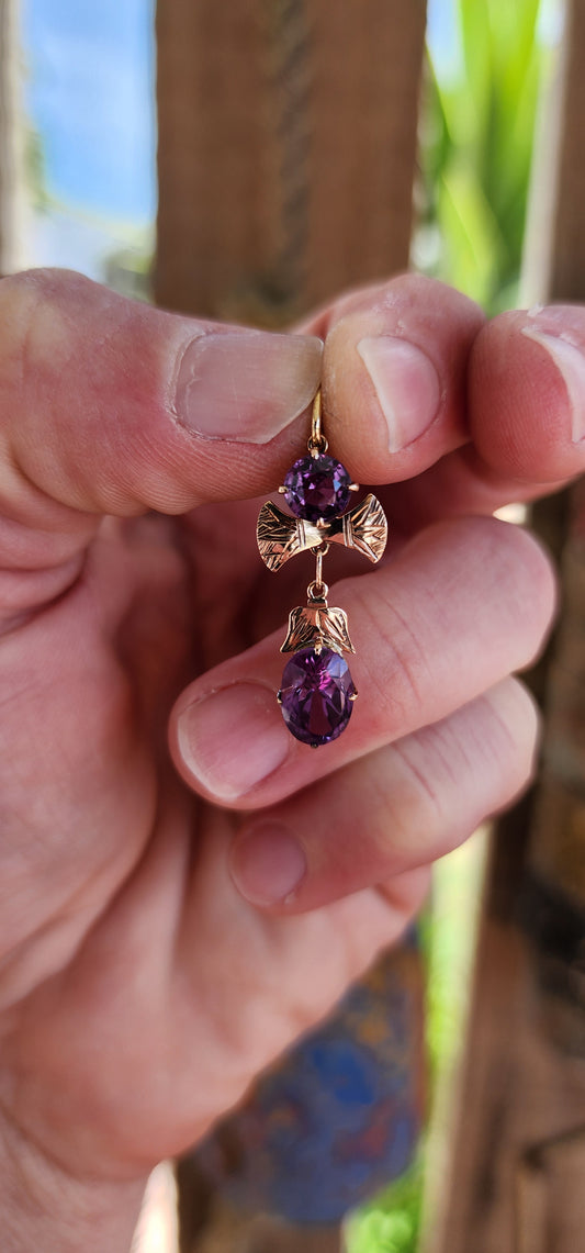 This is a beautiful vintage 9ct rose gold pendant set with lab-grown color-change sapphire gemstones. The design features two primary sapphires in a round and oval cut.