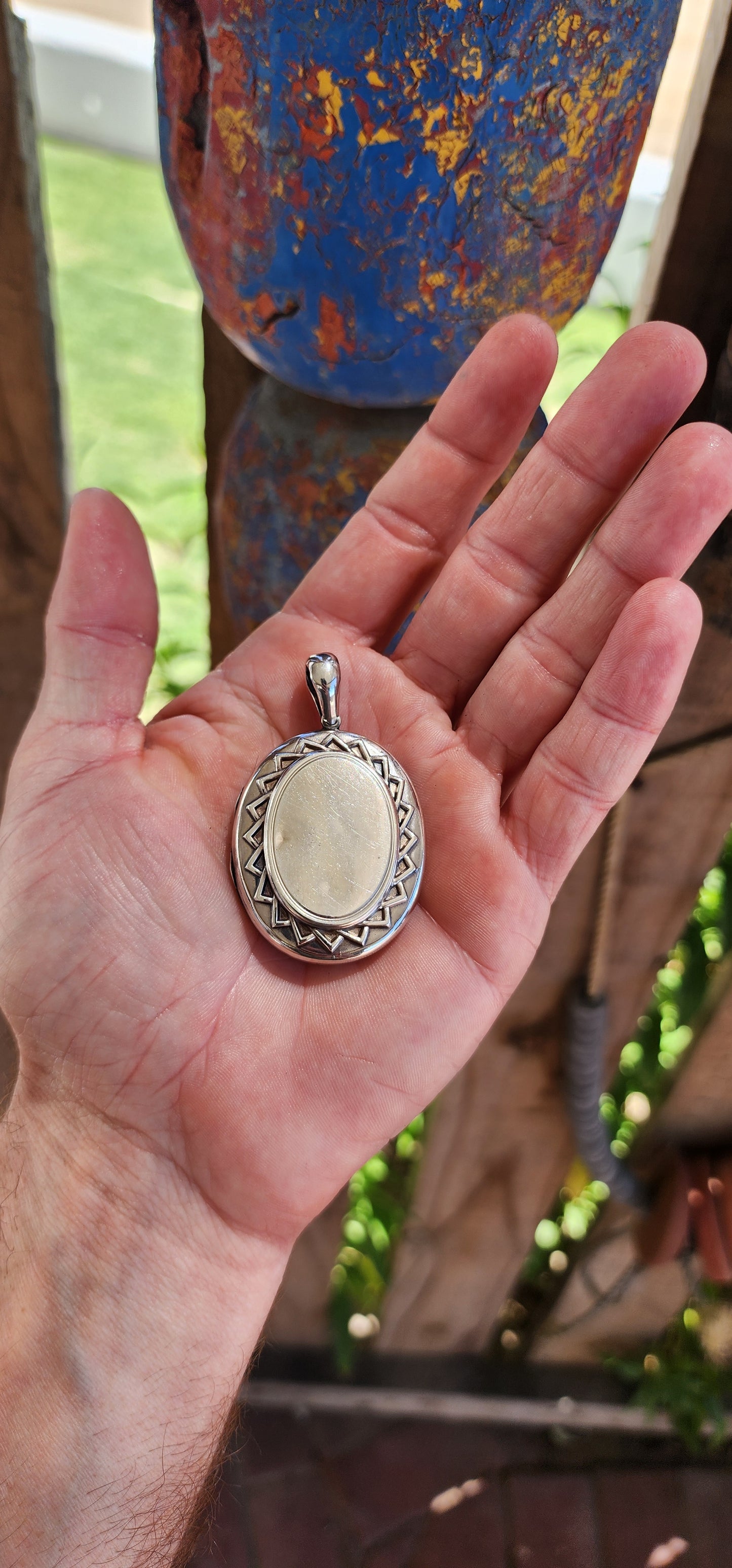 This large sized locket is a beautiful example of Victorian-era craftsmanship, designed in a sterling silver oval shape with a striking sunburst pattern encircling the center on both sides.