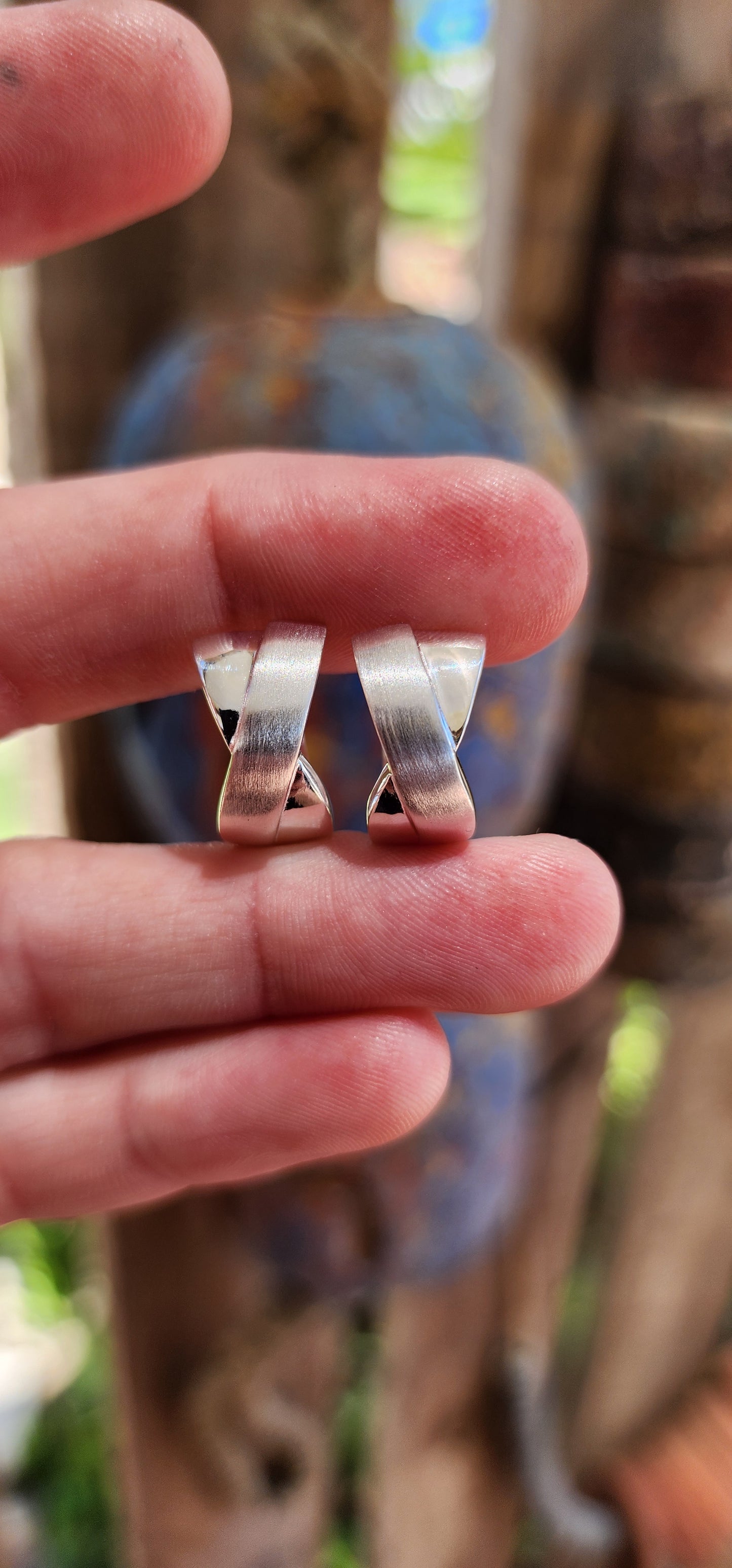 These stunning sterling silver huggie earrings are a masterpiece contemporary design. Their form exudes sophistication, featuring an X-shaped cross-over pattern that seamlessly combines polished silver with a soft, brushed texture.