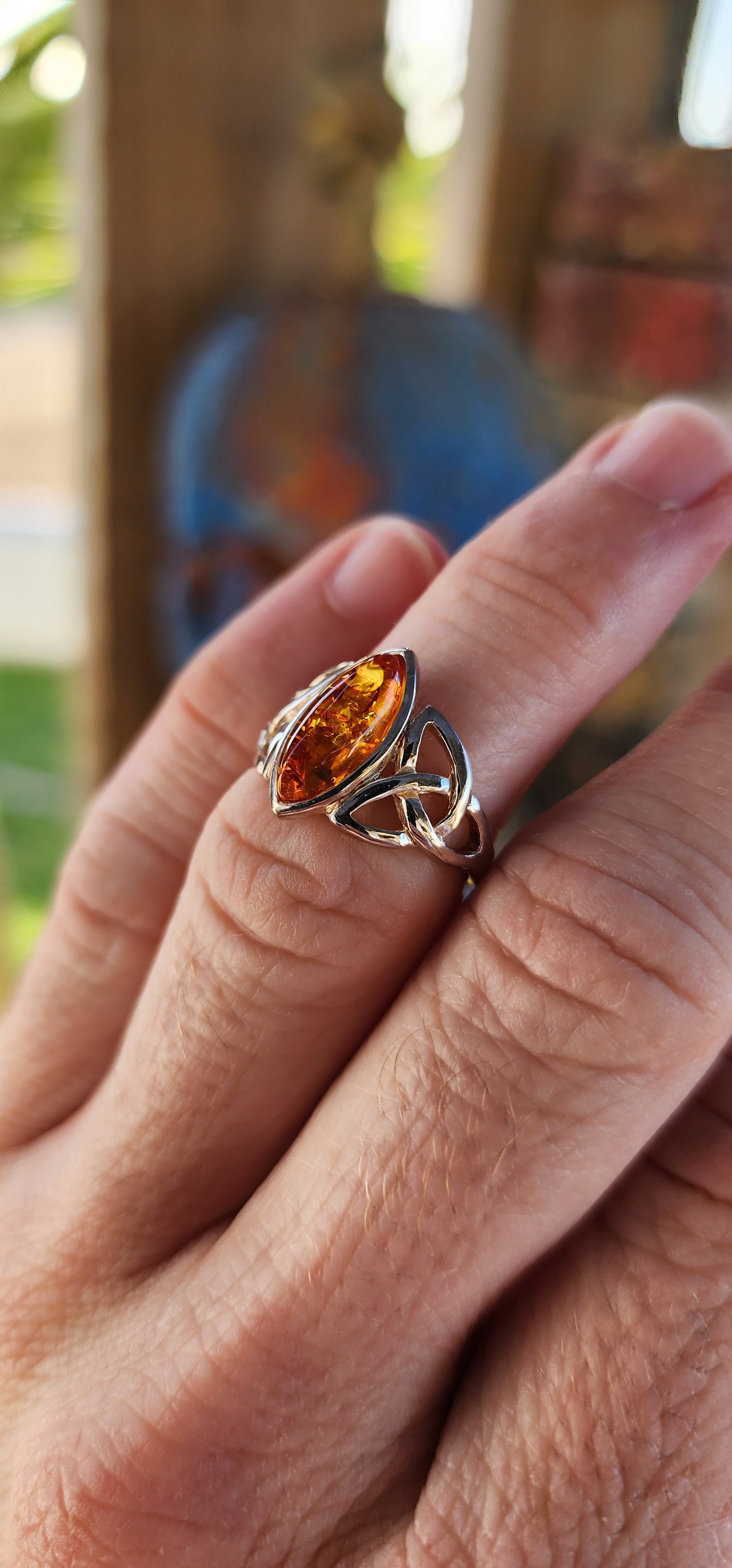 This sterling silver ring is a masterpiece of both elegance and symbolism, its design rooted in ancient Celtic tradition. At the heart of the piece rests a marquise-cut Baltic amber cabochon, its golden depths shimmering like liquid sunlight.