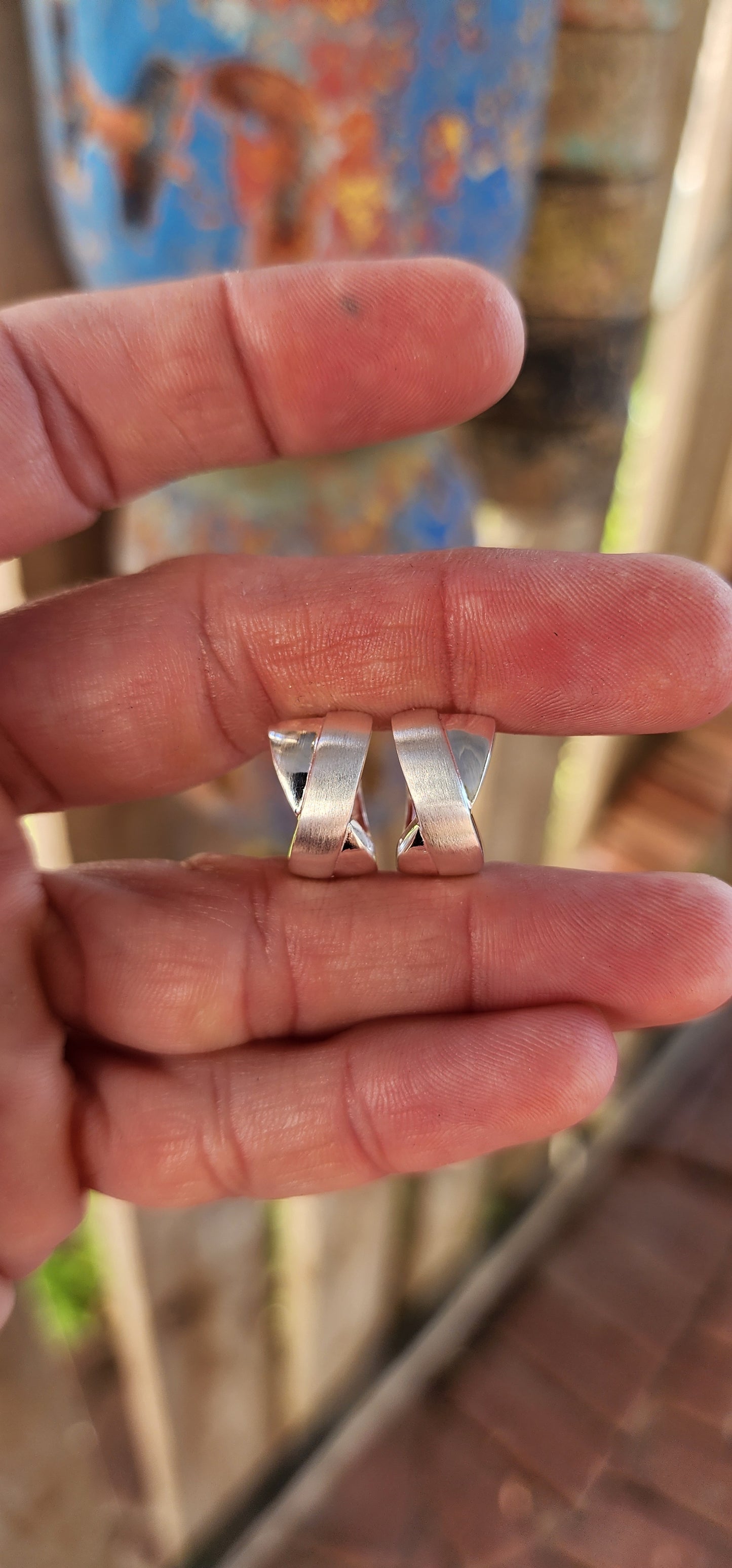 These stunning sterling silver huggie earrings are a masterpiece contemporary design. Their form exudes sophistication, featuring an X-shaped cross-over pattern that seamlessly combines polished silver with a soft, brushed texture.