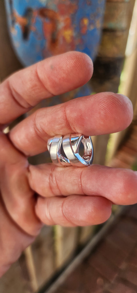 These stunning sterling silver huggie earrings are a masterpiece contemporary design. Their form exudes sophistication, featuring an X-shaped cross-over pattern that seamlessly combines polished silver with a soft, brushed texture.