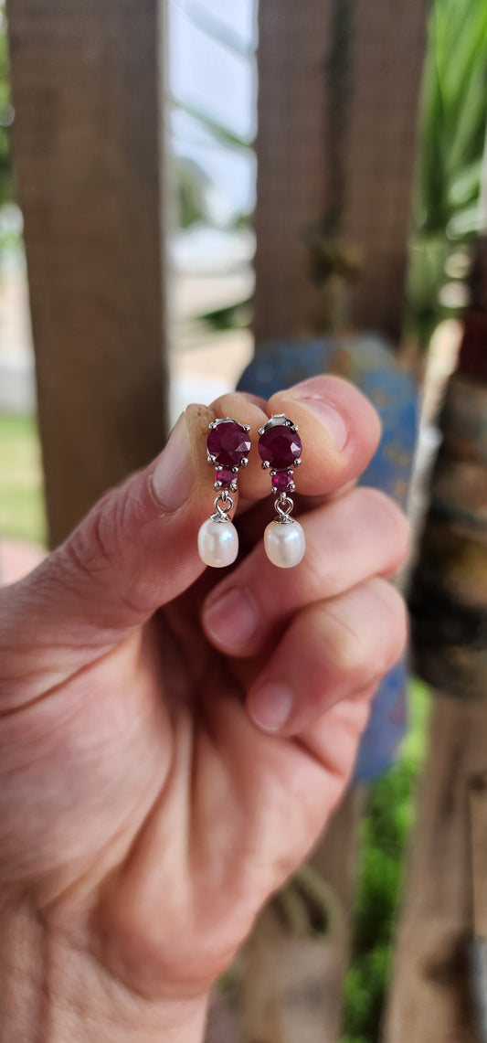 These radiant sterling silver earrings are a celebration of timeless romance .At their crown, each earring features a round-cut ruby in a rich, velvety crimson hue—expertly prong-set to capture and dance with the light like a spark from a royal hearth.