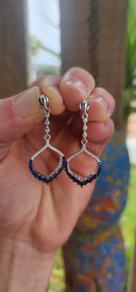 These dazzling drop earrings are where playful charm meets red carpet drama. Crafted in sleek, polished sterling silver, they feature an elegant vertical line of bezel-set clear round-cut cubic zirconia (CZ) gemstones, creating a graceful trail of sparkle