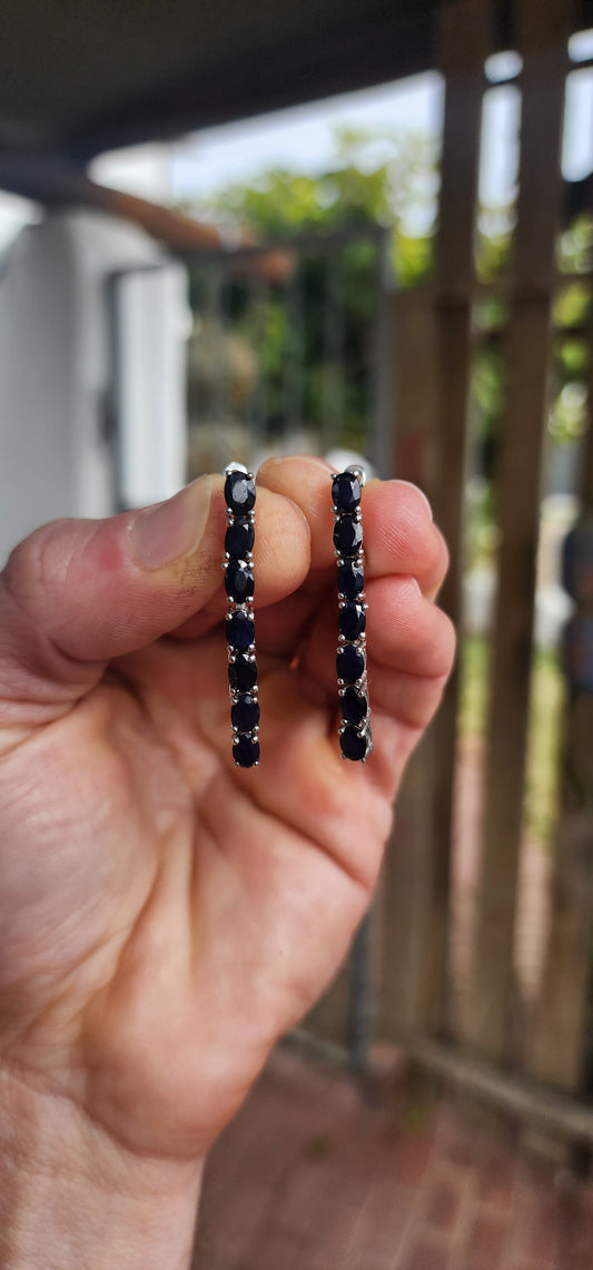 These sterling silver dangle earrings are designed to showcase the mysterious beauty of deep blue sapphires.