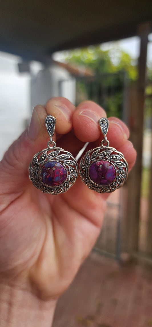 These earrings are little explosions of color and charm! Starting with a teardrop stud glimmering with marcasite sparkle, they cascade into a swirling silver flower/sunburst that frames a dazzling purple turquoise cabochon.