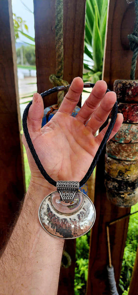 This is a bold, ethnic-inspired statement necklace that showcases a powerful artisanal aesthetic. The necklace centers on a dramatic pendant featuring a large, domed, oval-shaped disc crafted from hammered sterling silver.