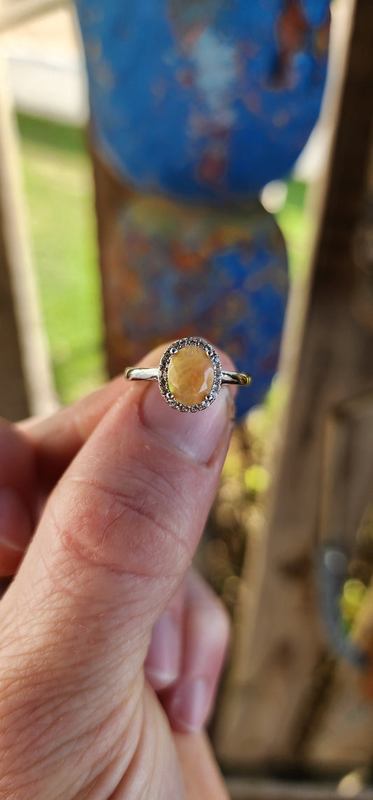 A timeless classic with a magical twist! This sterling silver beauty showcases a glowing orange oval-cut Ethiopian opal, prong set at the center where it shimmers with fiery flashes of orange, green, and golden yellow – like a sunset captured in stone.
