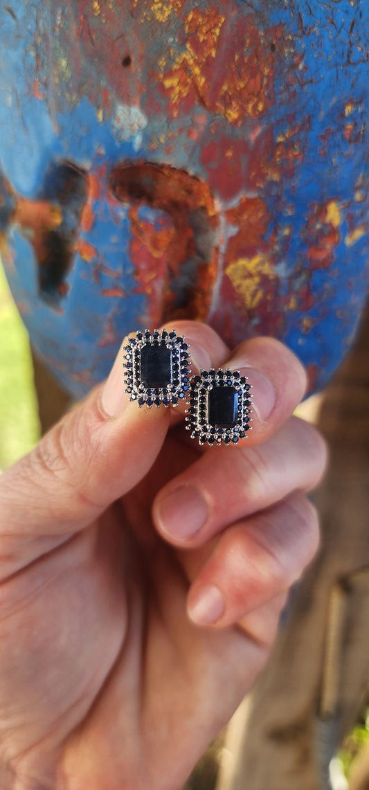 Striking and regal, these sterling silver stud earrings each feature a richly colored emerald-cut deep blue sapphire at the center.