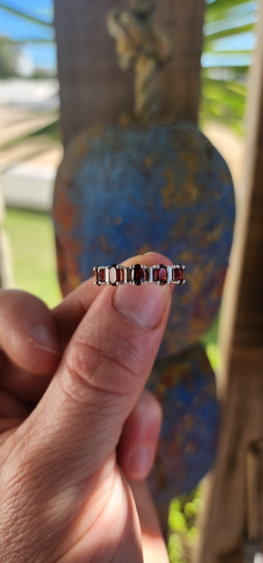 This sterling silver half-eternity ring is a timeless and elegant piece, featuring five richly hued oval-cut garnet gemstones.