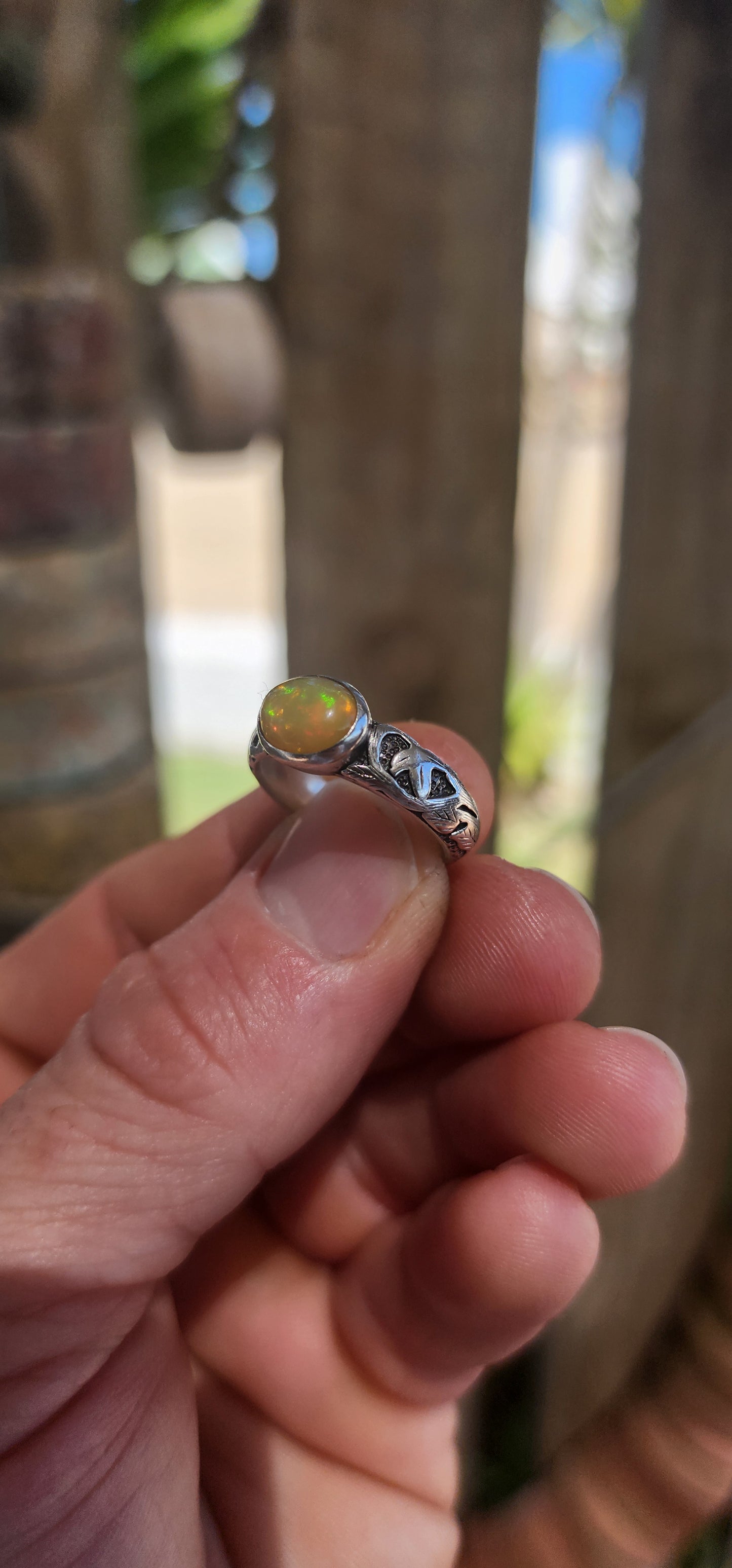 An absolutely mesmerizing handcrafted sterling silver ring featuring a luminous oval-cut Ethiopian fire opal cabochon, radiating with flickers of neon green, orange, and gold as it catches the light.