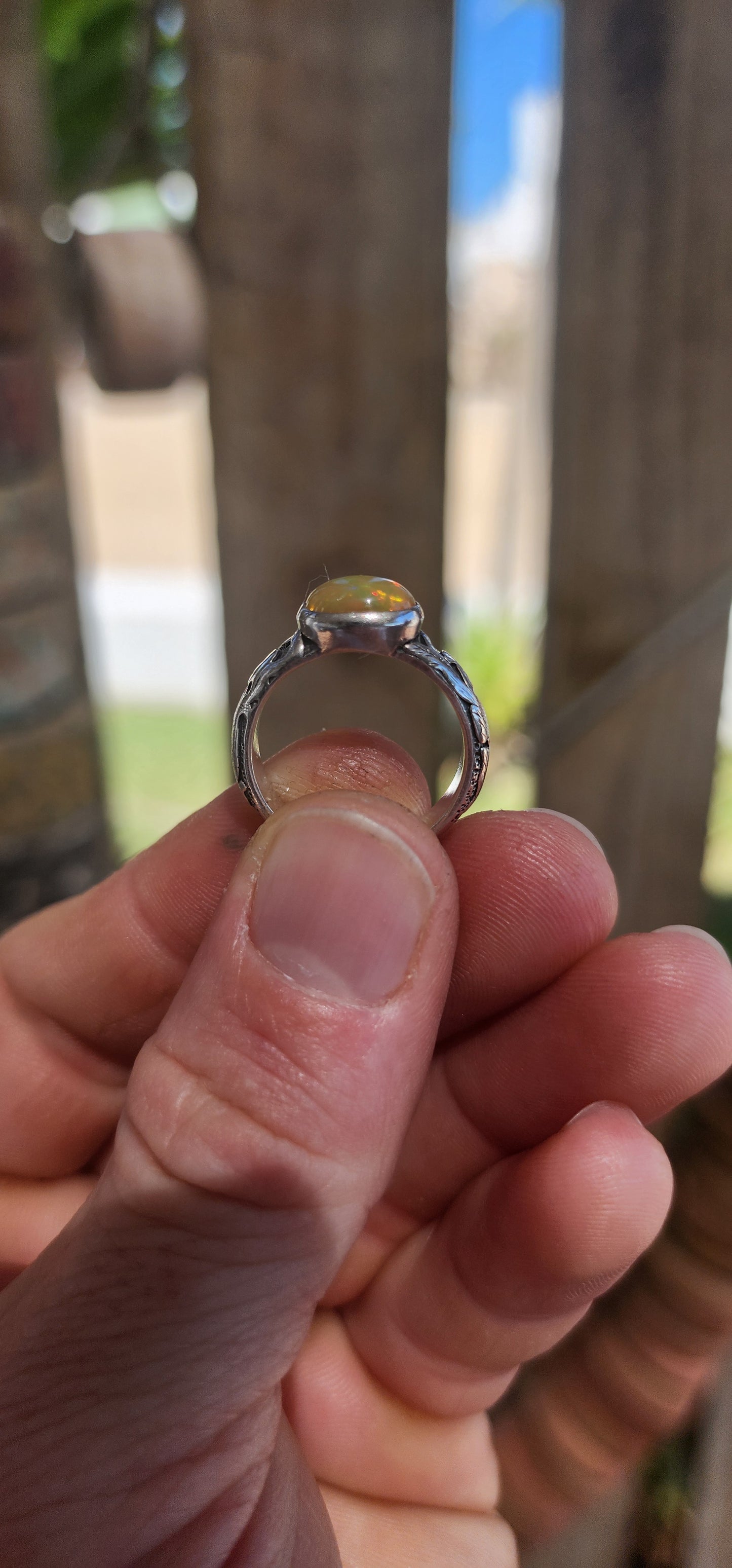 An absolutely mesmerizing handcrafted sterling silver ring featuring a luminous oval-cut Ethiopian fire opal cabochon, radiating with flickers of neon green, orange, and gold as it catches the light.