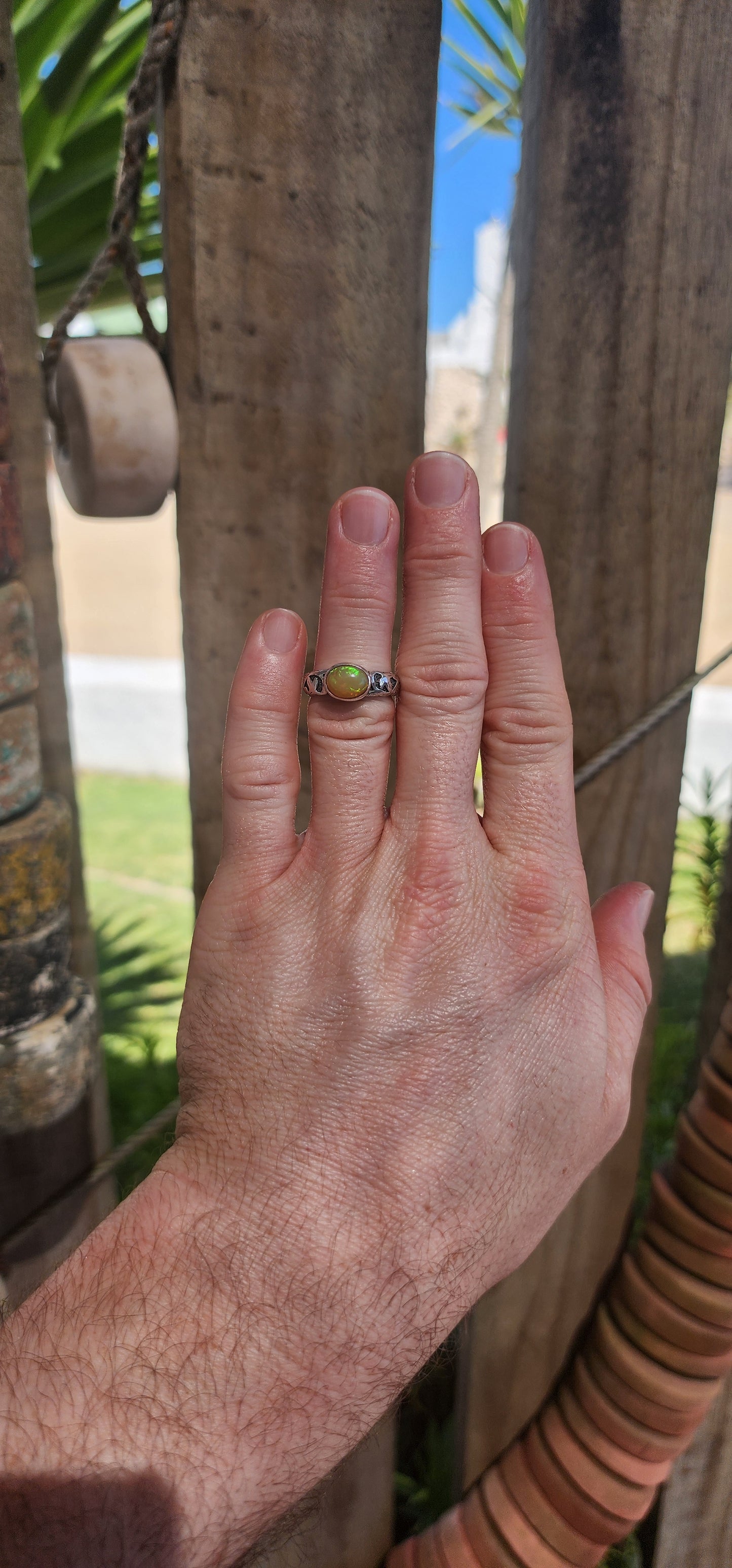 An absolutely mesmerizing handcrafted sterling silver ring featuring a luminous oval-cut Ethiopian fire opal cabochon, radiating with flickers of neon green, orange, and gold as it catches the light.