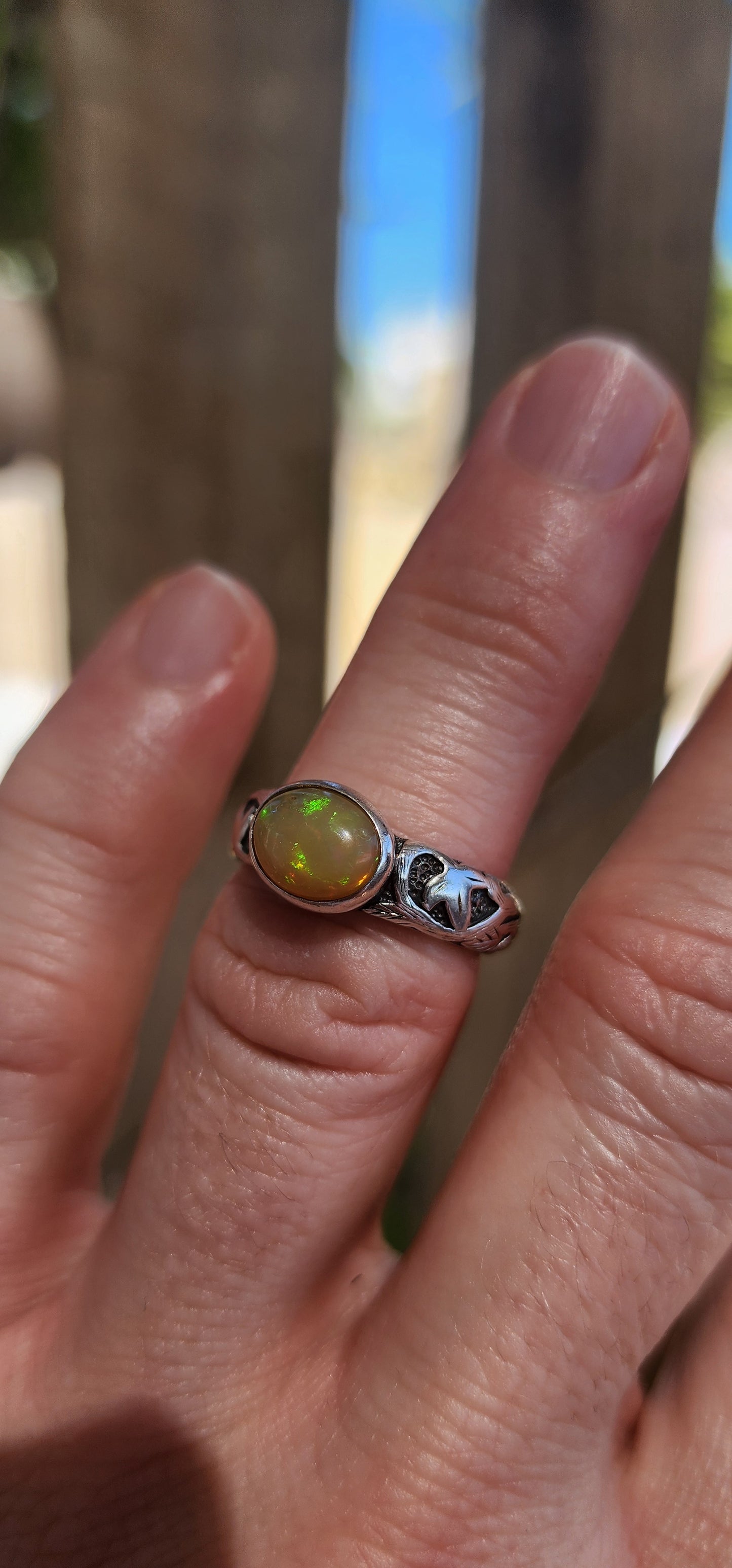 An absolutely mesmerizing handcrafted sterling silver ring featuring a luminous oval-cut Ethiopian fire opal cabochon, radiating with flickers of neon green, orange, and gold as it catches the light.