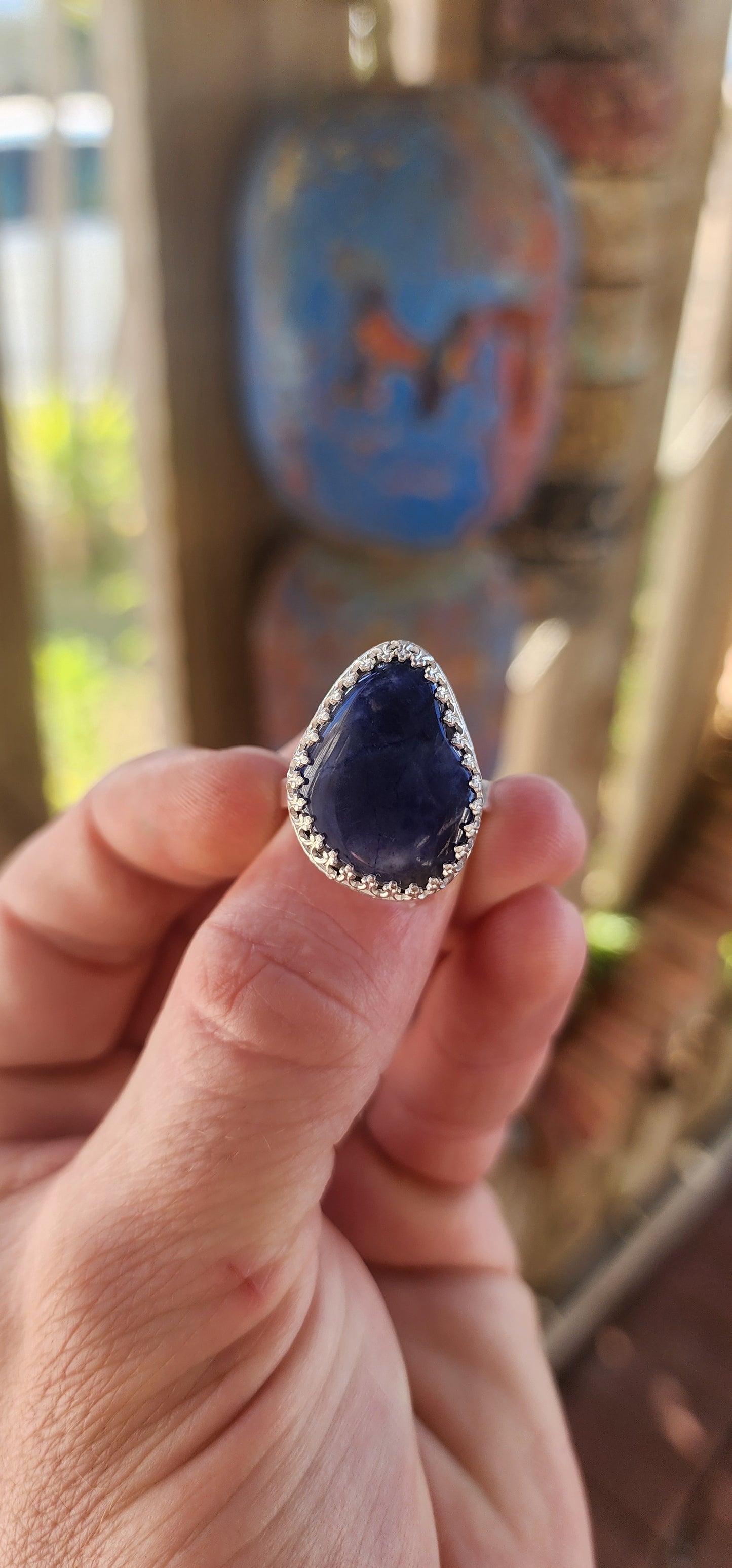 This artisan made sterling silver ring features a tumbled, organic-shaped blue sodalite gemstone, bezel-like cradled in ornate decorative claw prongs that look like a little crown around the stone.