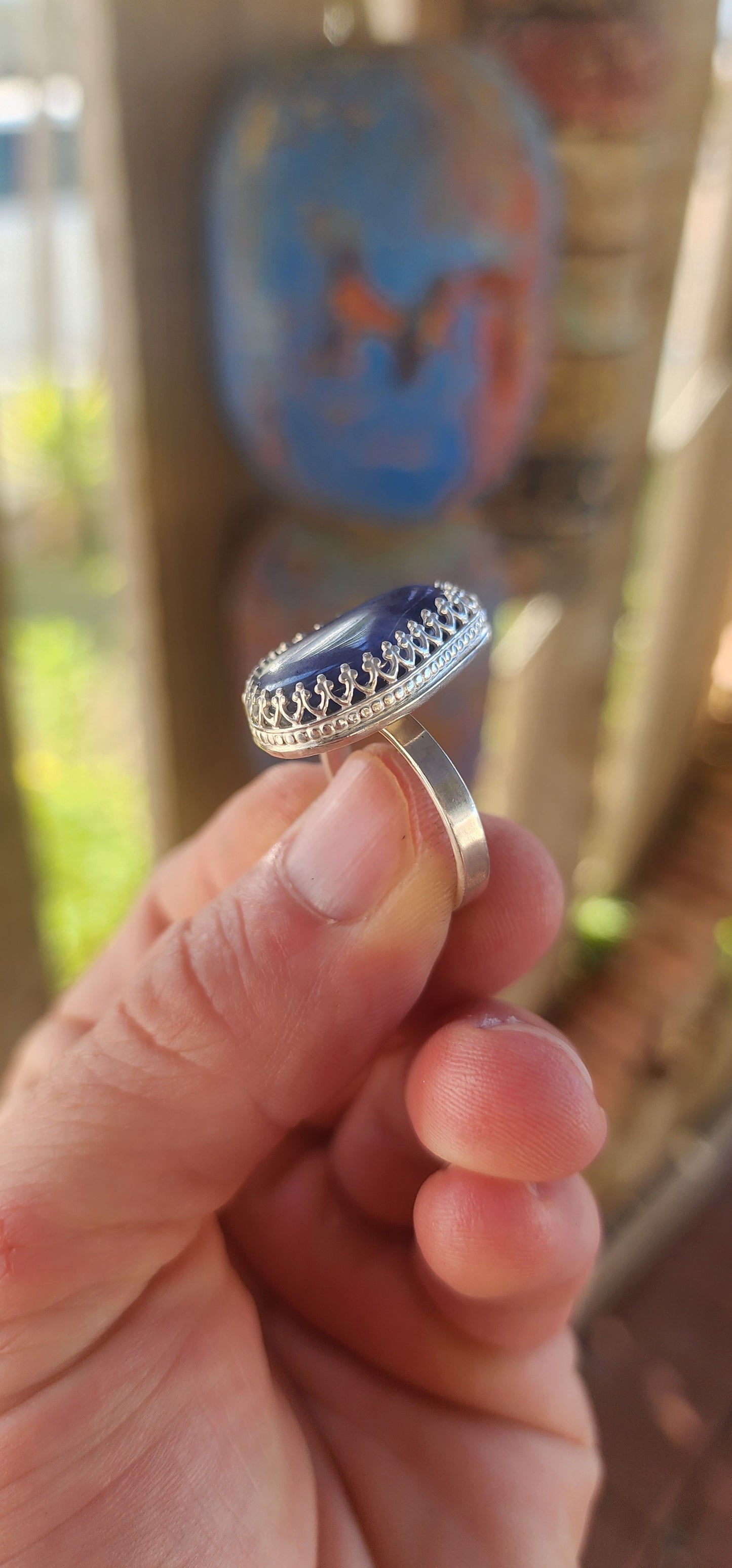 This artisan made sterling silver ring features a tumbled, organic-shaped blue sodalite gemstone, bezel-like cradled in ornate decorative claw prongs that look like a little crown around the stone.