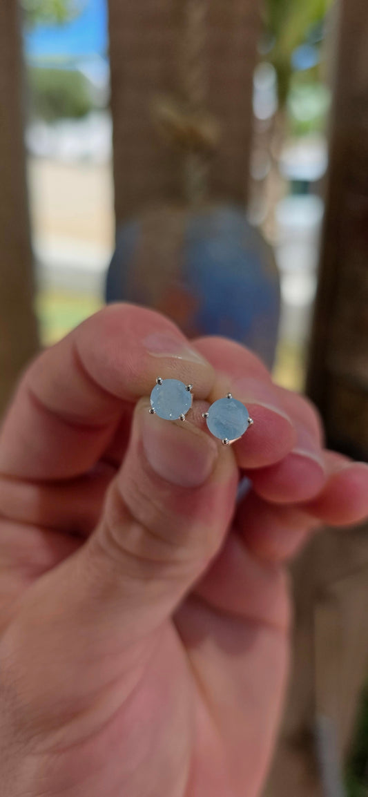 This striking pair of unisex sterling silver stud earrings features round faceted aquamarine gemstones in a soft milky / opaque tone — giving them a dreamy, sea-glass quality rather than a fully transparent sparkle.