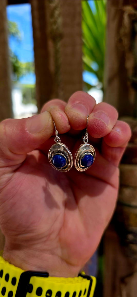 This striking pair of sterling silver dangle earrings features an oval-shaped, layered frame design, each centred with a rich royal-blue lapis lazuli cabochon.