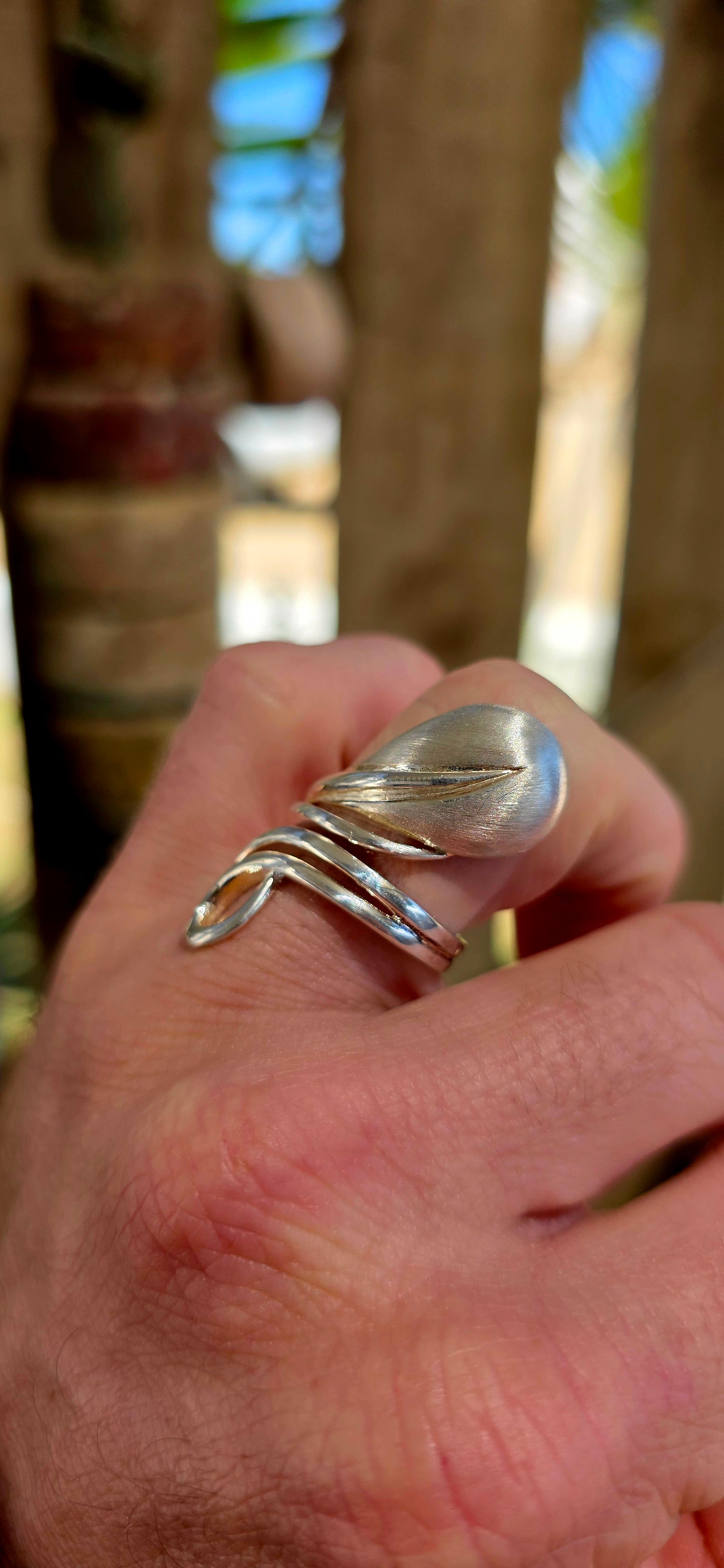 This striking artisan-made ring is crafted in solid sterling silver and designed in a dramatic modernist wrap style, where flowing silver forms curl gracefully around the finger like a ribbon of metal.