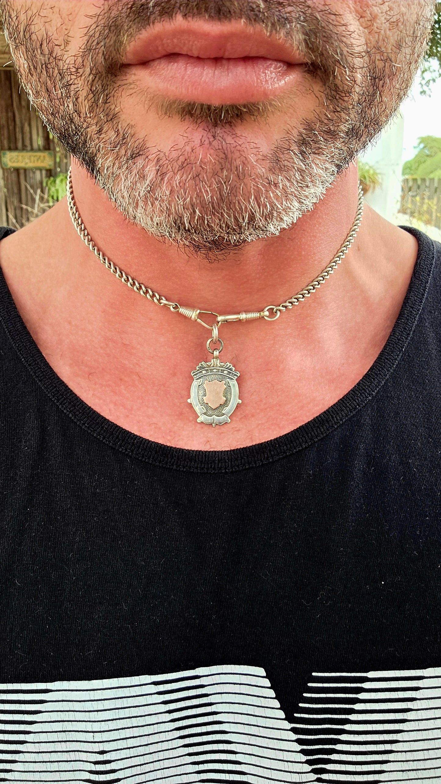 This beautiful antique shield fob pendant is crafted in hallmarked sterling silver, featuring a striking 9ct rose gold shield cartouche at its centre.