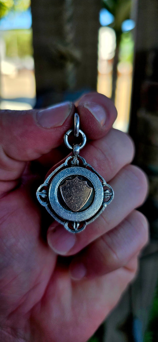 A beautiful antique hallmarked fob shield pendant, crafted in sterling silver and decorated with a raised 9ct rose gold shield cartouche, creating a striking and elegant two-tone contrast.