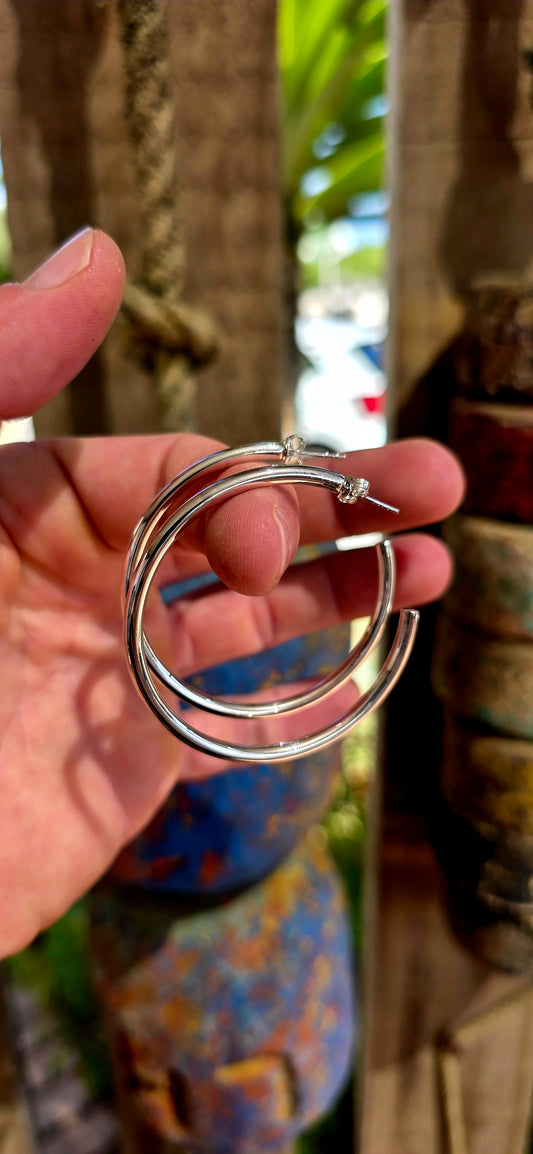 These are proper statement hoops — a generously sized pair crafted in sterling silver, designed in a classic round tubular (hollow) form that gives you that big, bold look without the heavy weight.