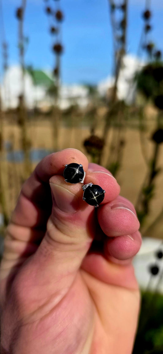 Unisex pair of sterling silver stud earrings with luxurious rhodium plating for a bright tarnish-resistant finish, each prong set with a genuine rare black star diopside cabochon gemstone.