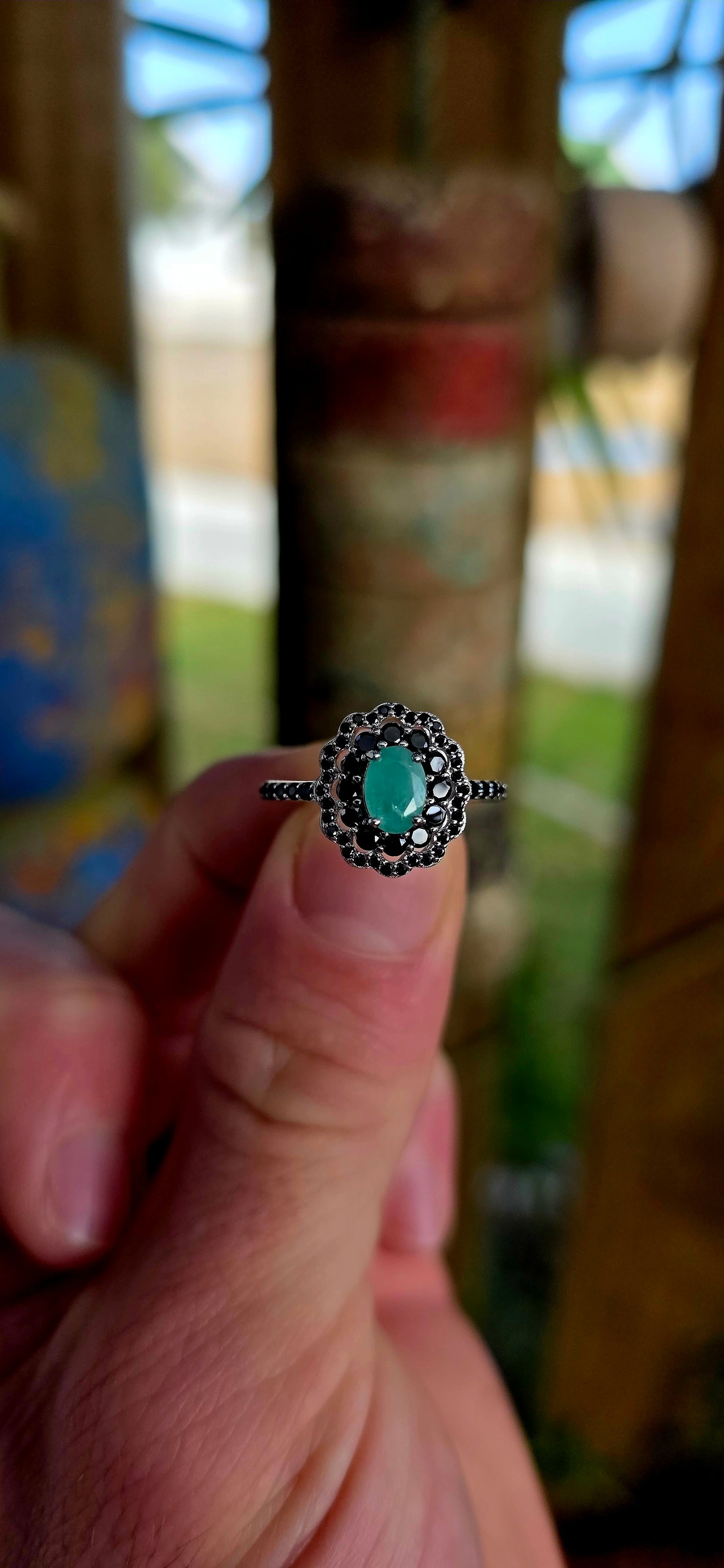 Beautiful matching sterling silver floral-inspired ring and earring set featuring luminous oval-cut emerald gemstones at their centres, each delicately prong set and framed in dramatic double scalloped halos of sparkling black spinel gemstones.