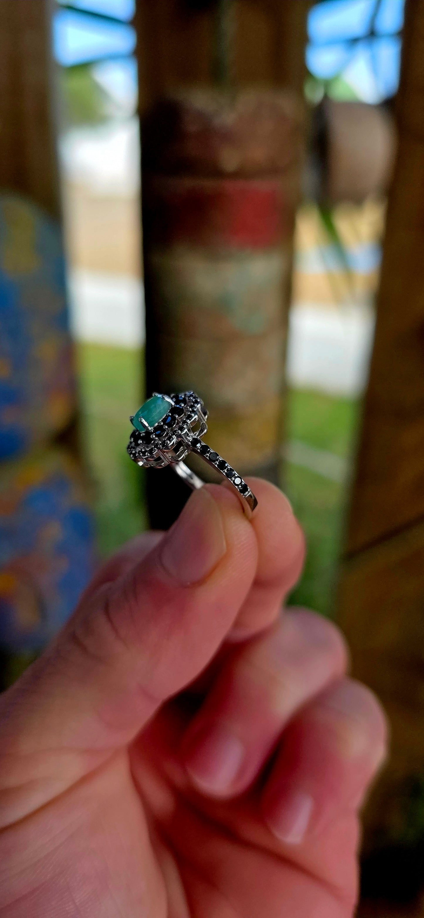 Beautiful matching sterling silver floral-inspired ring and earring set featuring luminous oval-cut emerald gemstones at their centres, each delicately prong set and framed in dramatic double scalloped halos of sparkling black spinel gemstones.