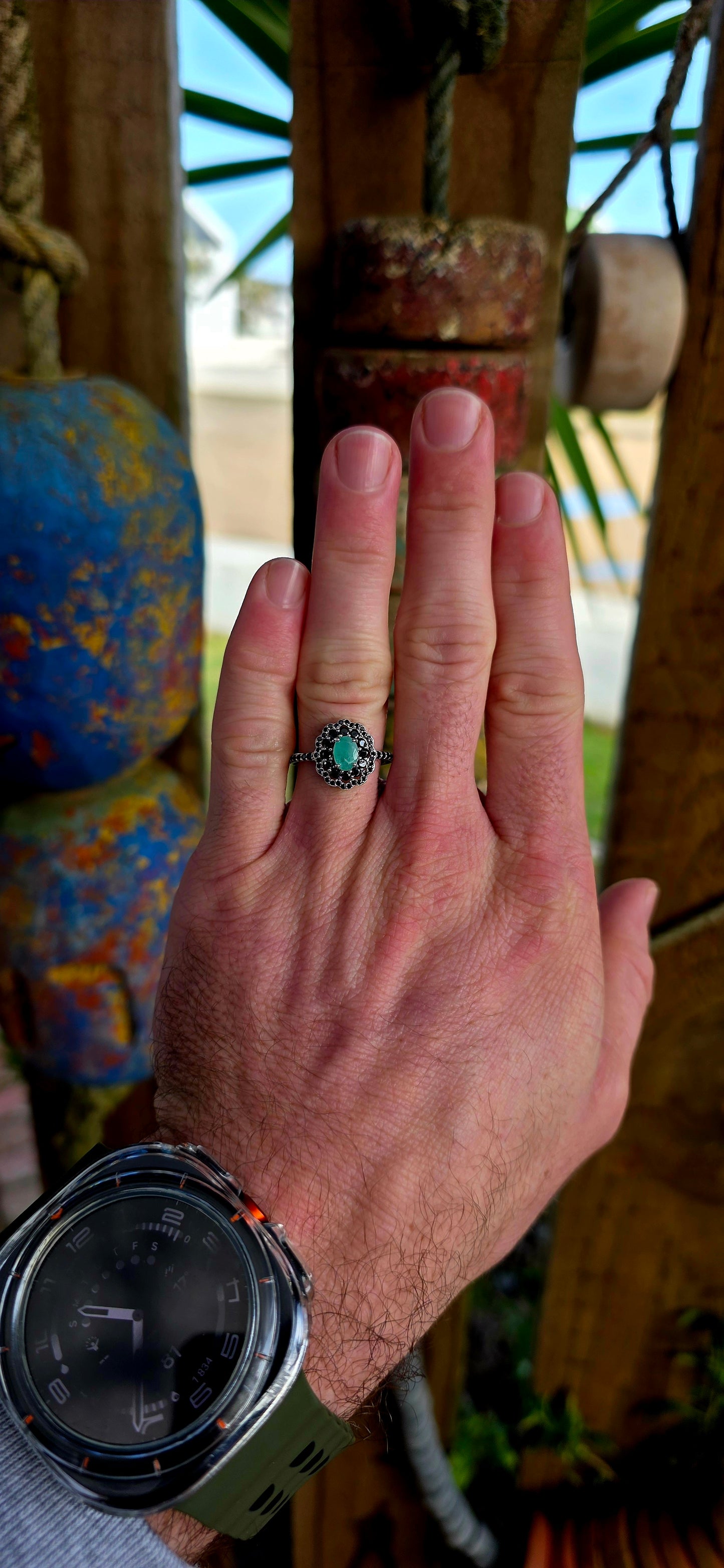 Beautiful matching sterling silver floral-inspired ring and earring set featuring luminous oval-cut emerald gemstones at their centres, each delicately prong set and framed in dramatic double scalloped halos of sparkling black spinel gemstones.