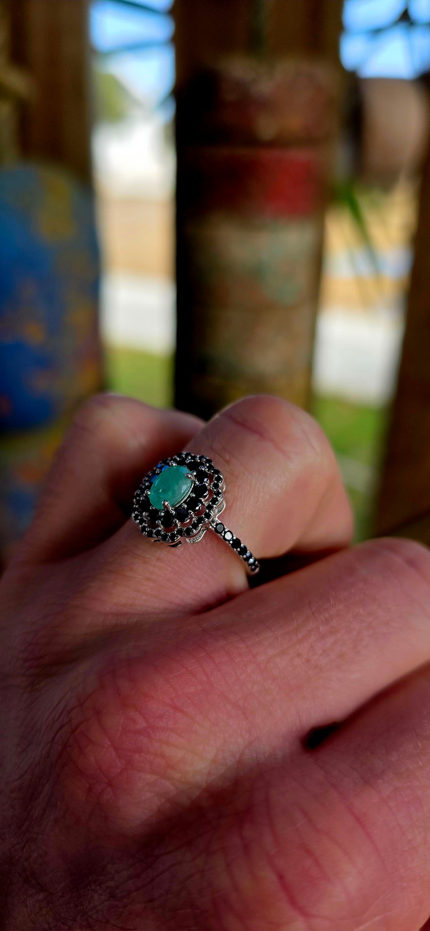 Beautiful matching sterling silver floral-inspired ring and earring set featuring luminous oval-cut emerald gemstones at their centres, each delicately prong set and framed in dramatic double scalloped halos of sparkling black spinel gemstones.