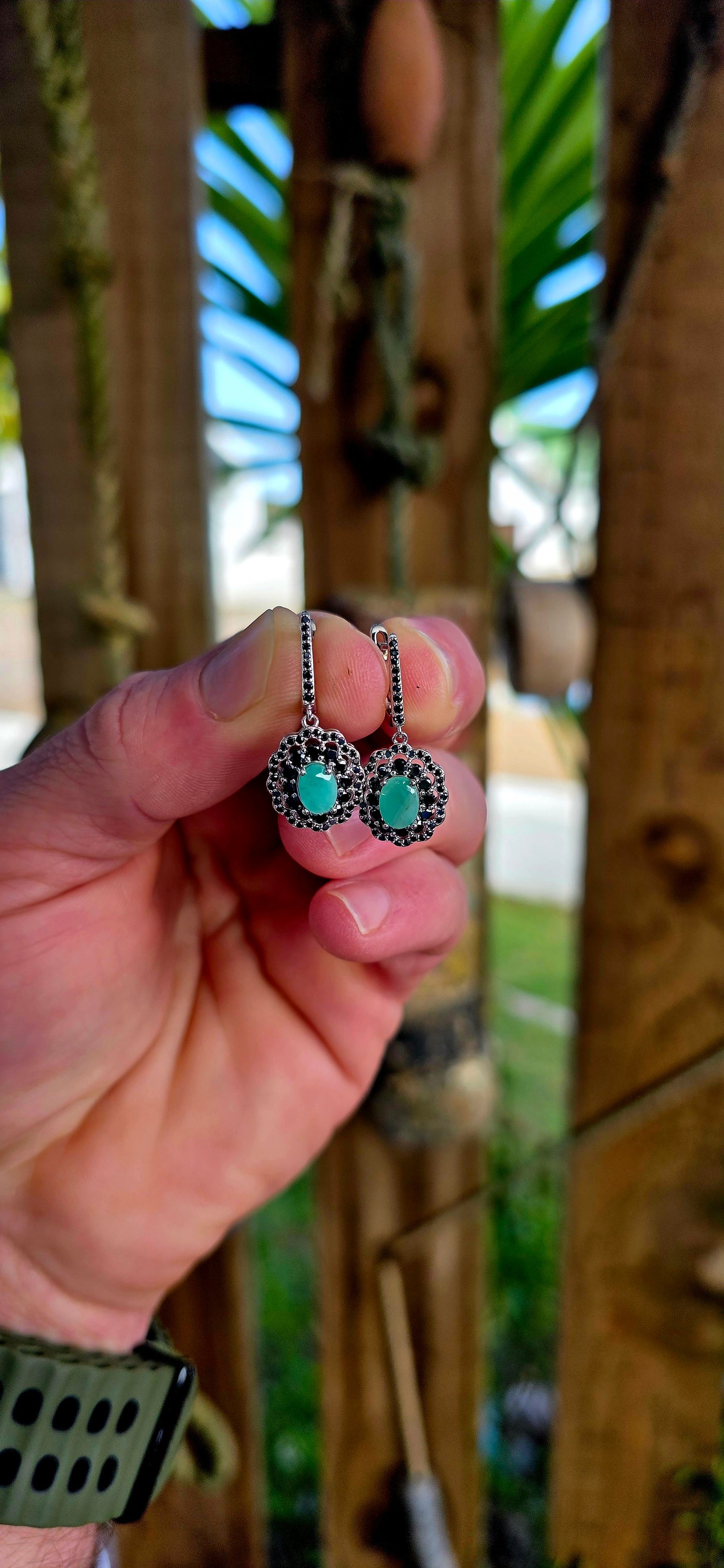 Beautiful matching sterling silver floral-inspired ring and earring set featuring luminous oval-cut emerald gemstones at their centres, each delicately prong set and framed in dramatic double scalloped halos of sparkling black spinel gemstones.