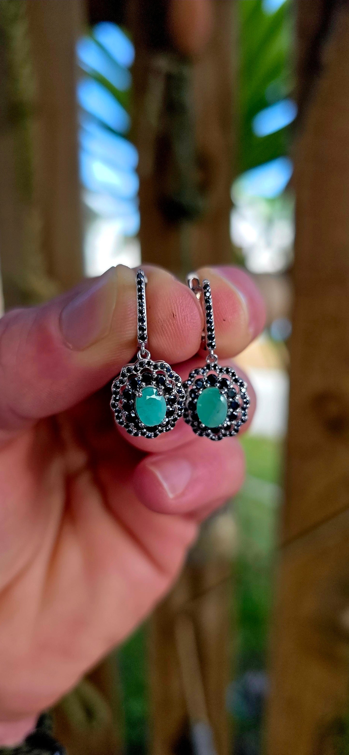 Beautiful matching sterling silver floral-inspired ring and earring set featuring luminous oval-cut emerald gemstones at their centres, each delicately prong set and framed in dramatic double scalloped halos of sparkling black spinel gemstones.