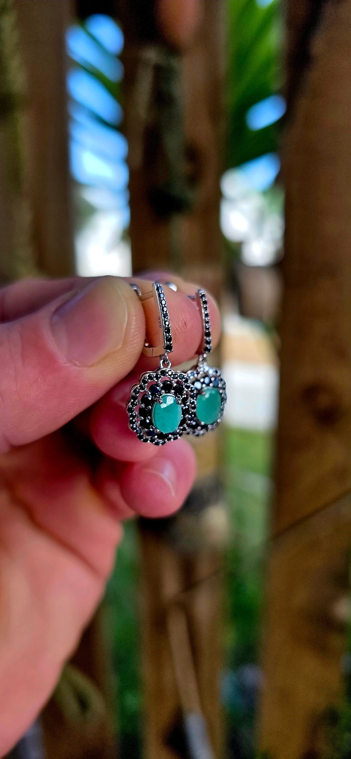 Beautiful matching sterling silver floral-inspired ring and earring set featuring luminous oval-cut emerald gemstones at their centres, each delicately prong set and framed in dramatic double scalloped halos of sparkling black spinel gemstones.