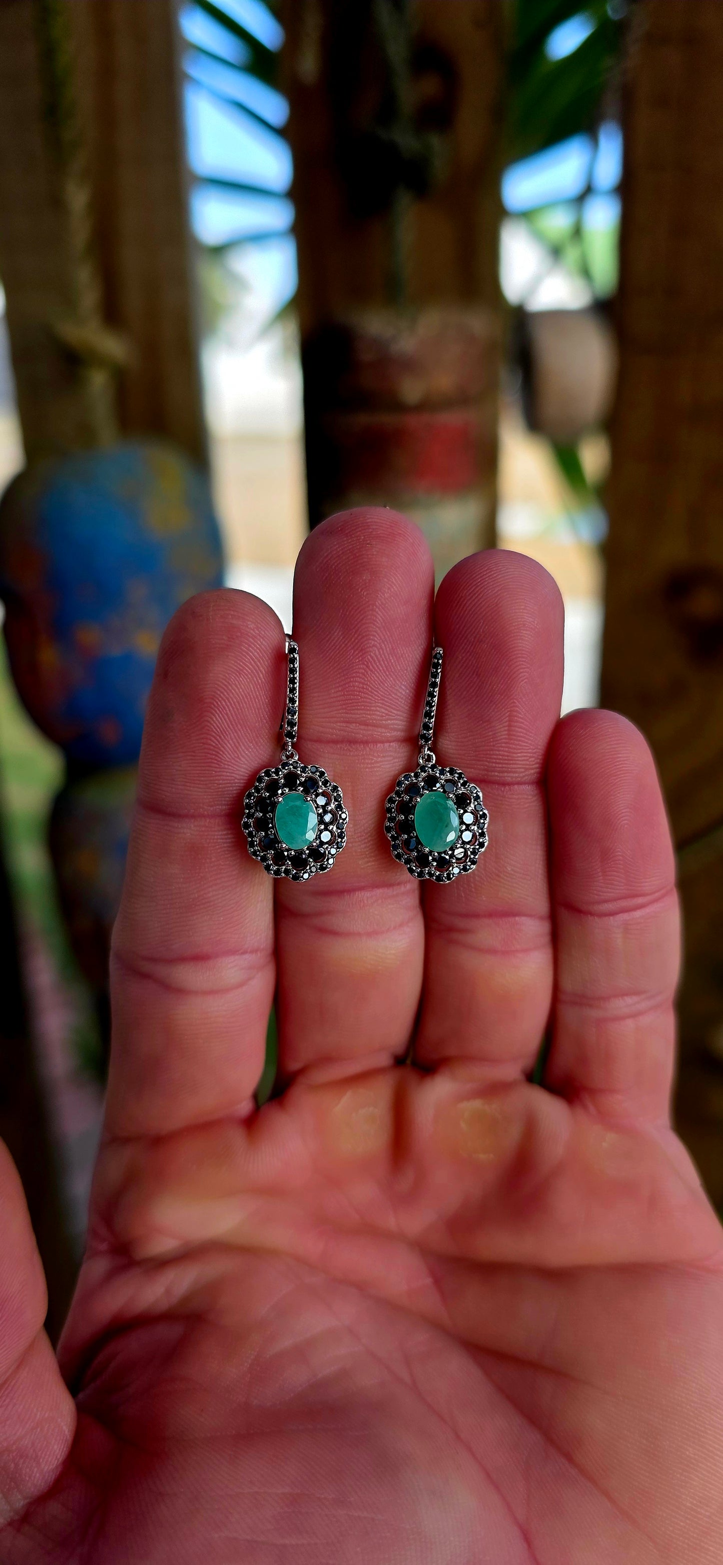 Beautiful matching sterling silver floral-inspired ring and earring set featuring luminous oval-cut emerald gemstones at their centres, each delicately prong set and framed in dramatic double scalloped halos of sparkling black spinel gemstones.