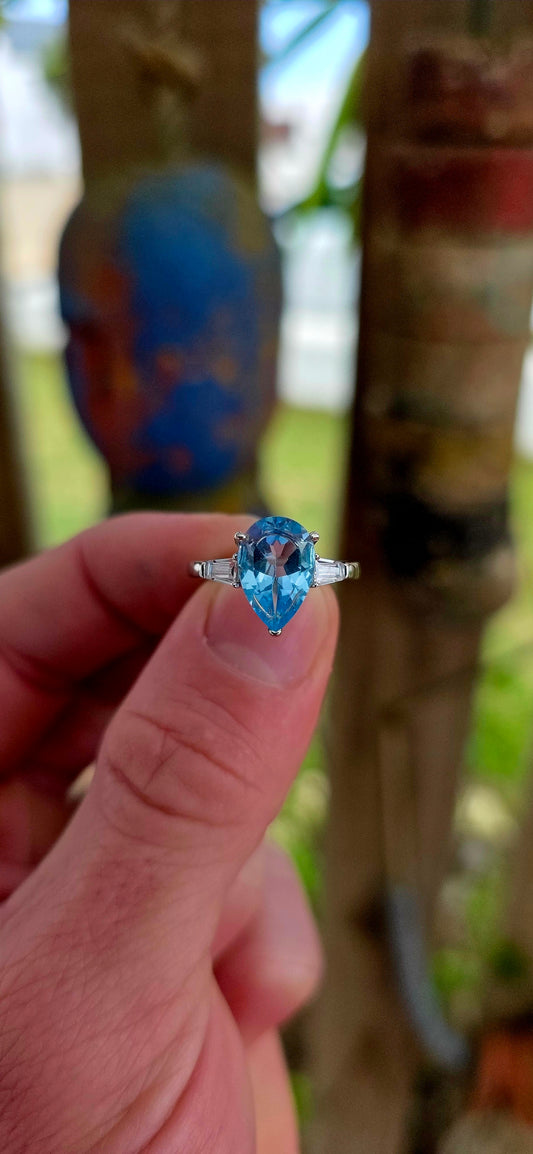 This elegant Art Deco revival trilogy ring is crafted in sterling silver and crowned with a generously sized pear-cut Swiss blue topaz in a classic prong setting.