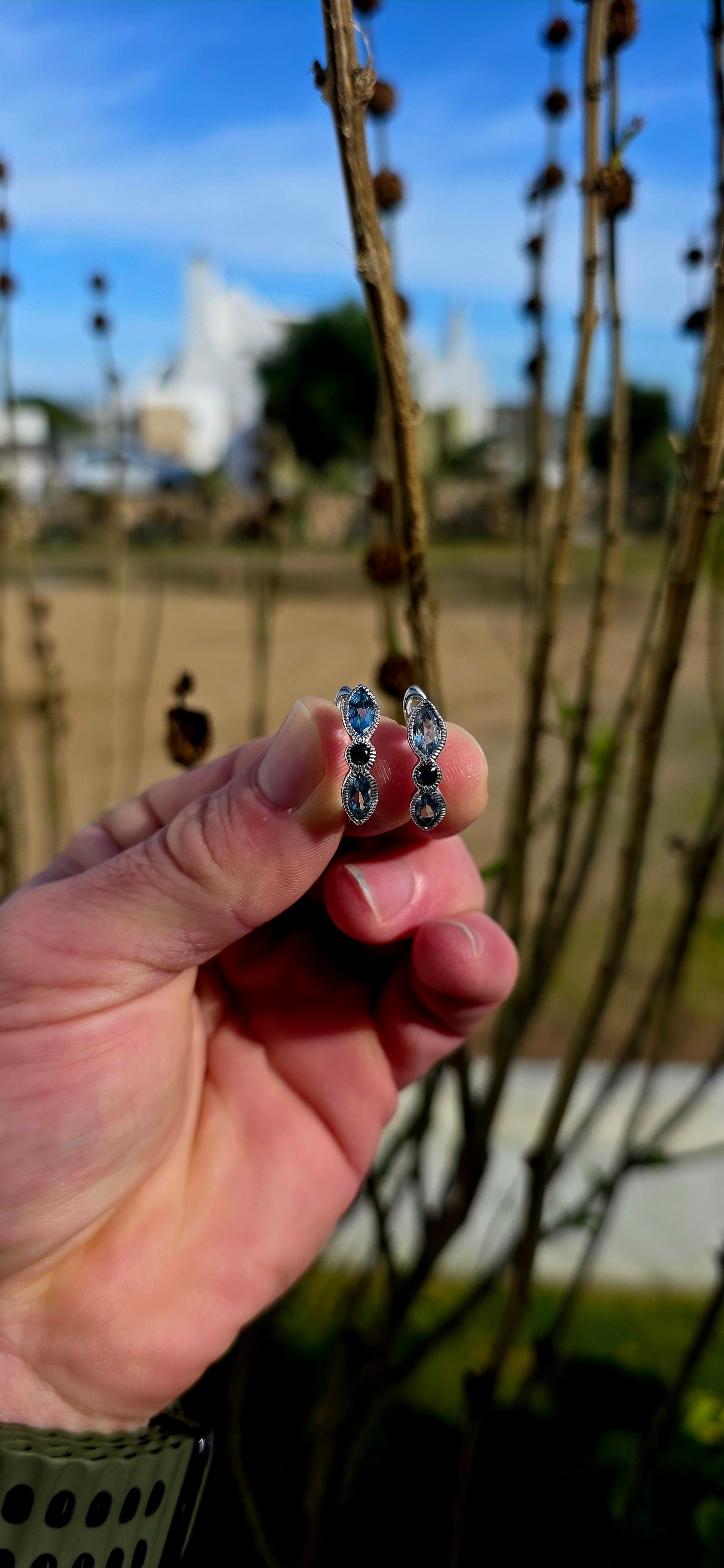 Crafted in sterling silver, these beautiful half-hoop dress earrings feature a graceful vertical arrangement of faceted marquise-cut sky blue topaz gemstones, separated by a rich dark blue round-cut sapphire at the centre.