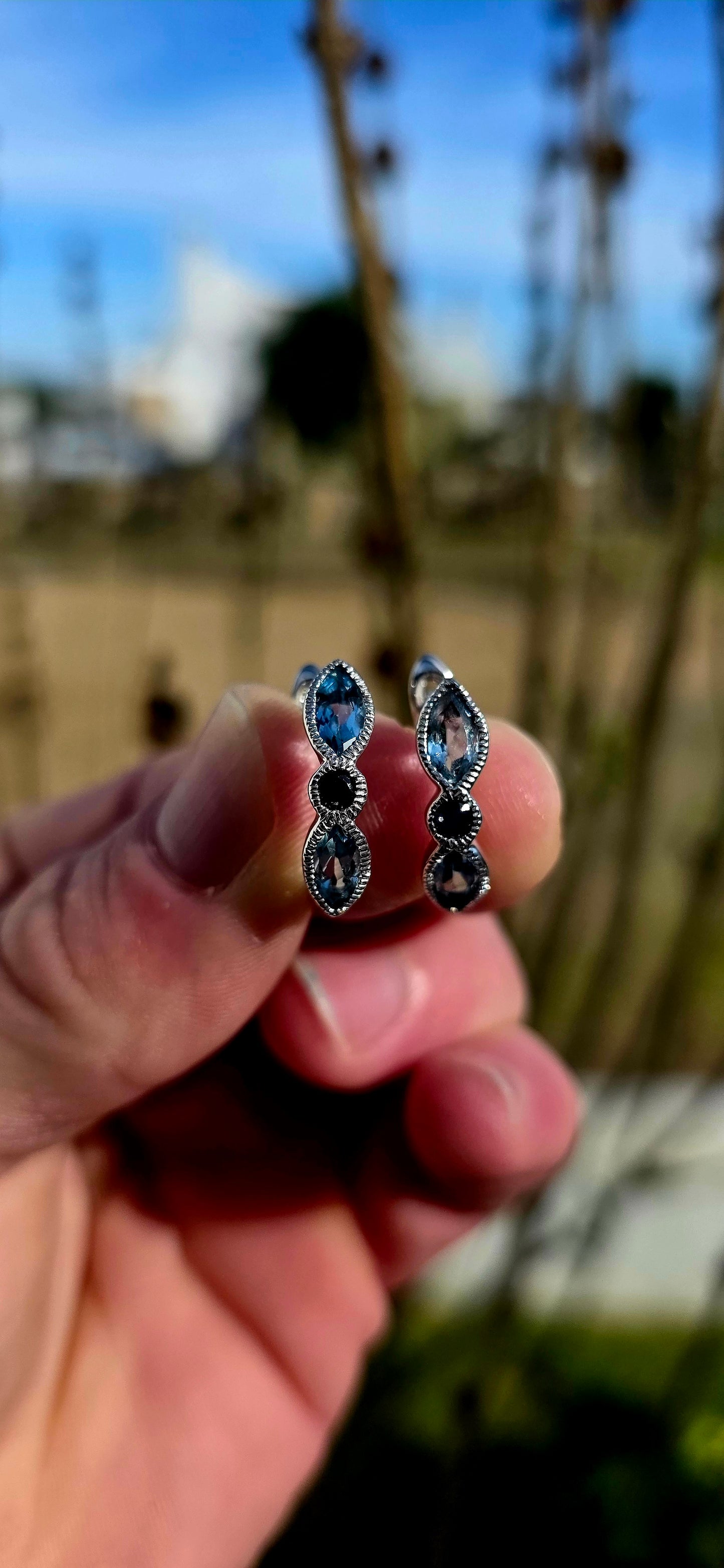 Crafted in sterling silver, these beautiful half-hoop dress earrings feature a graceful vertical arrangement of faceted marquise-cut sky blue topaz gemstones, separated by a rich dark blue round-cut sapphire at the centre.