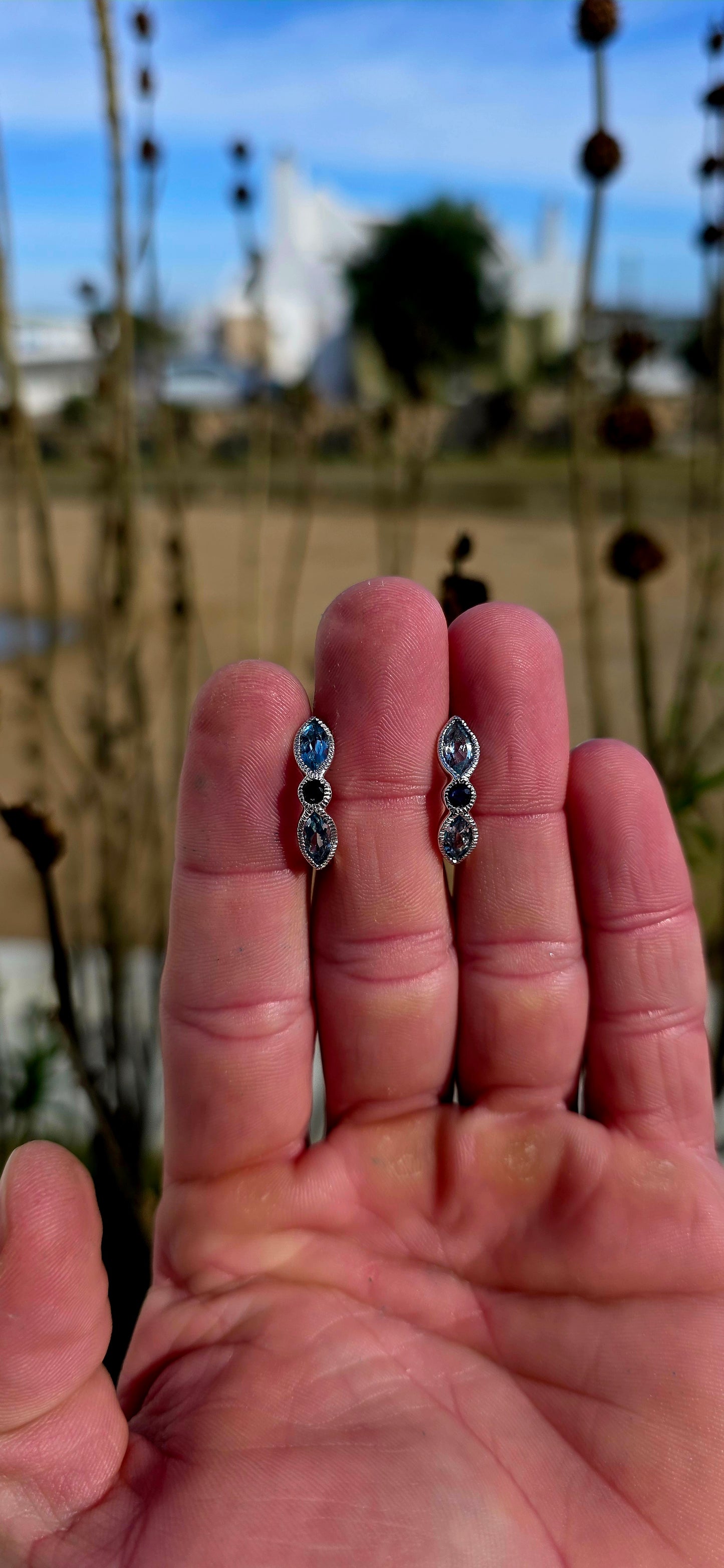 Crafted in sterling silver, these beautiful half-hoop dress earrings feature a graceful vertical arrangement of faceted marquise-cut sky blue topaz gemstones, separated by a rich dark blue round-cut sapphire at the centre.
