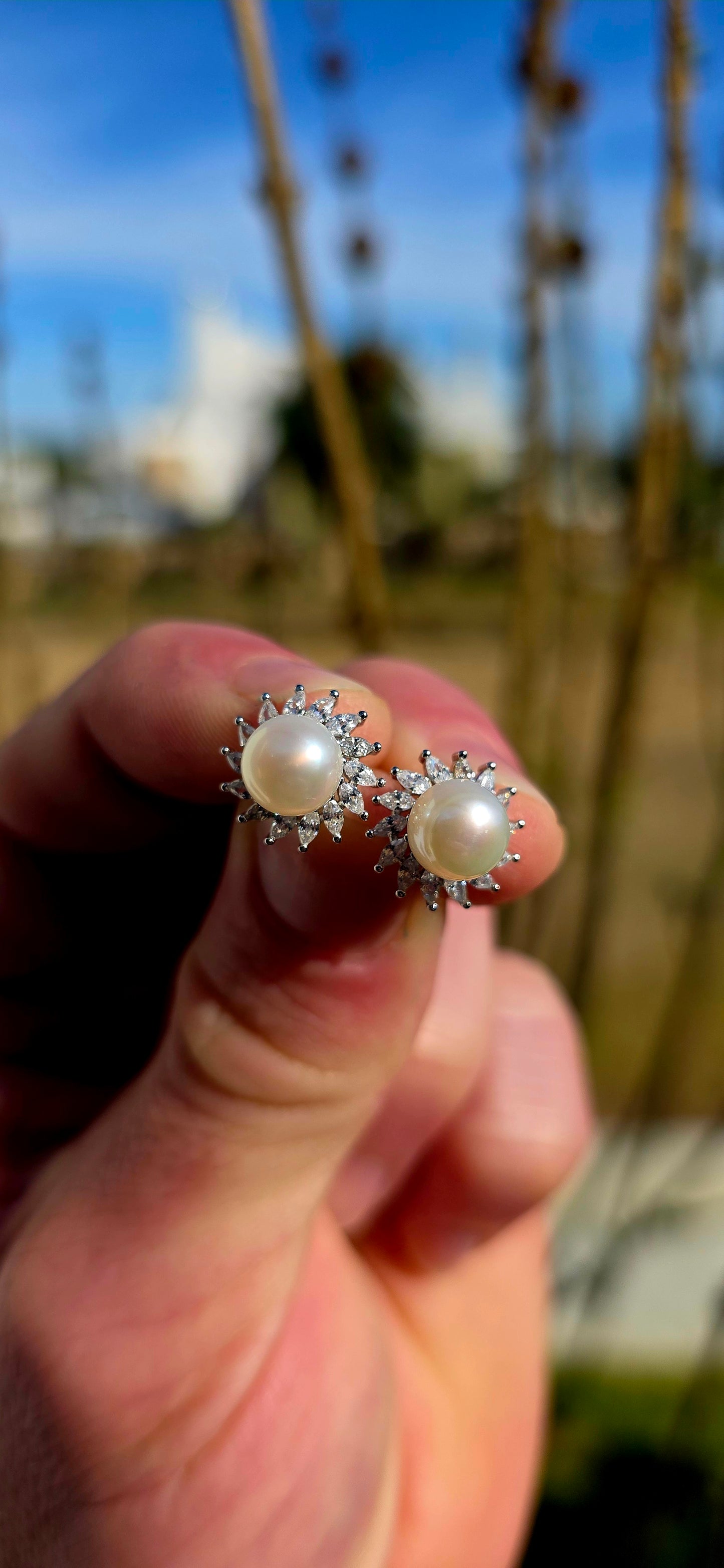 These elegant and beautifully classic sterling silver stud earrings each feature a luminous freshwater pearl at the centre, framed in a radiant halo of marquise-cut cubic zirconia gemstones in delicate prong settings.
